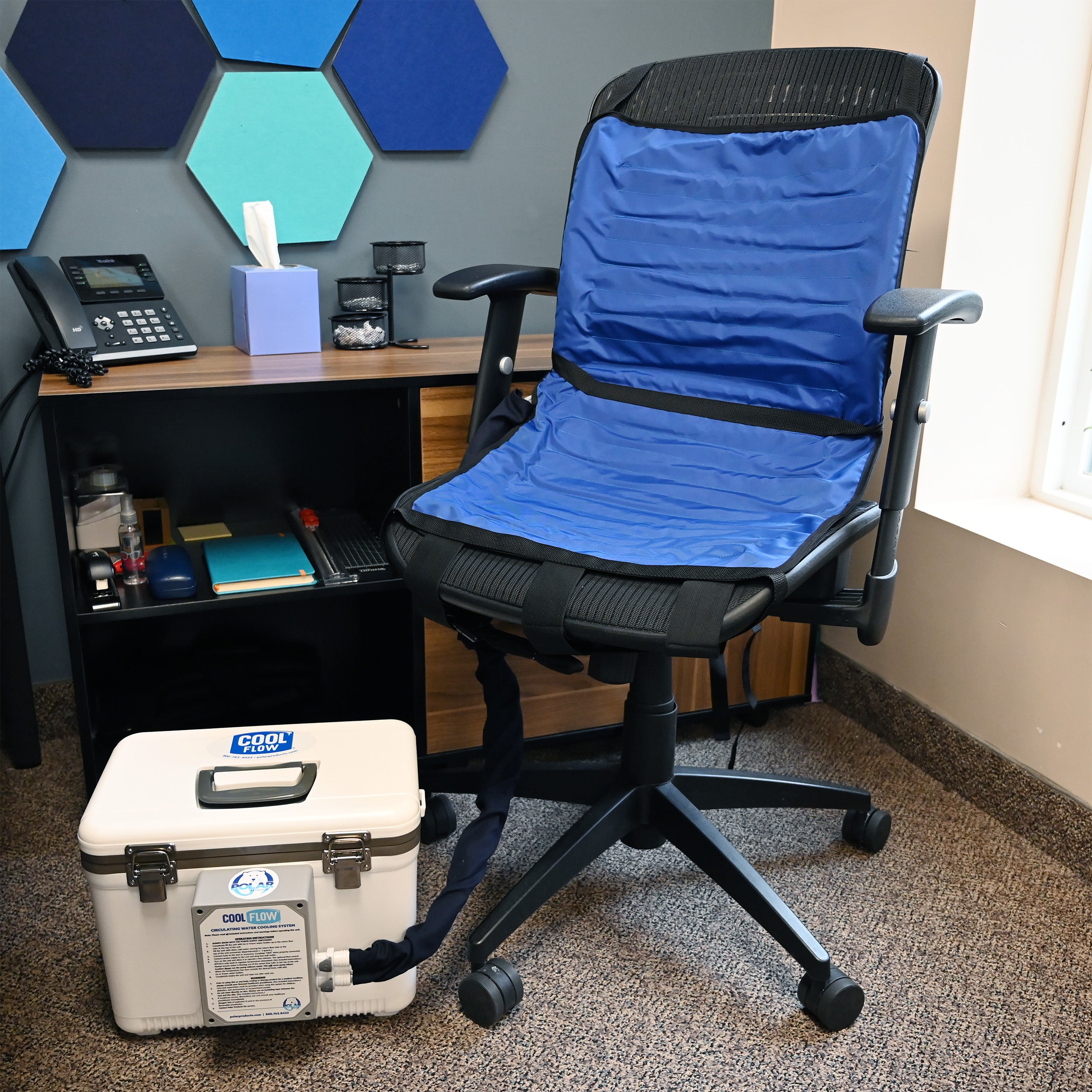 A blue and black circulating cooling seat set up on a black office chair, with a white insulated 13-quart cooling reservoir connected by a navy hose to the chair's cooling system.