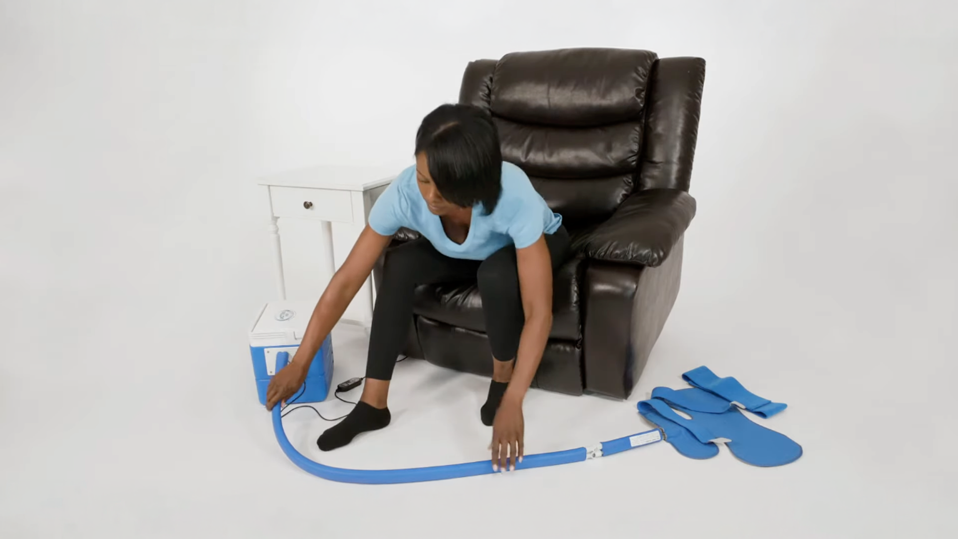 Person connecting a broad shoulder therapy pad to their 9-quart active ice® 3.0 cold therapy system while sitting on a brown leather recliner, with a white background.
