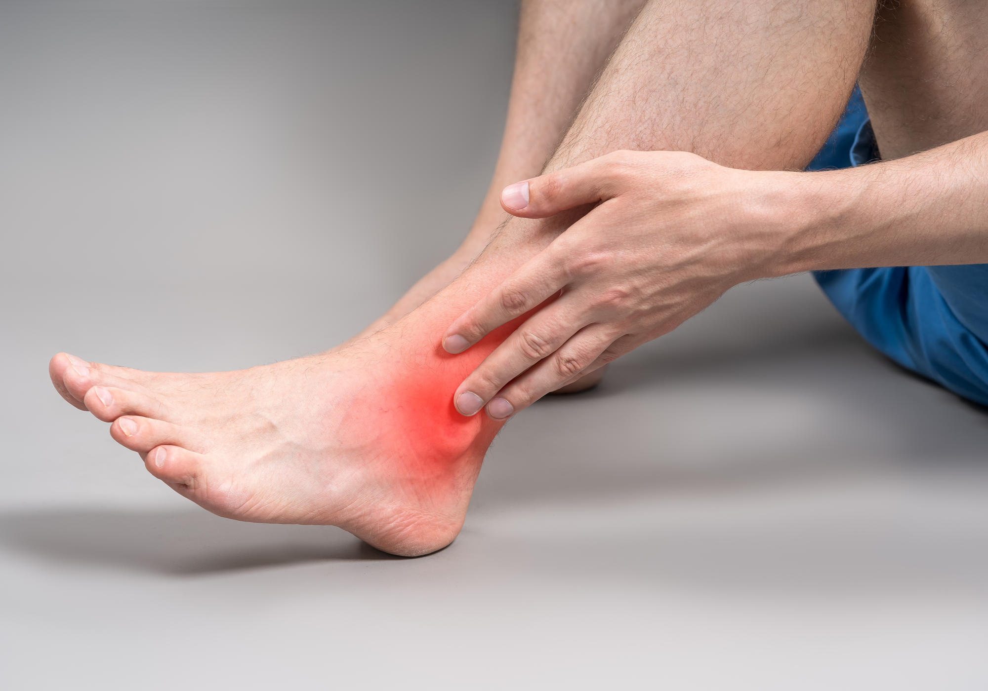 Person holding a painful foot with red highlighting on a gray background