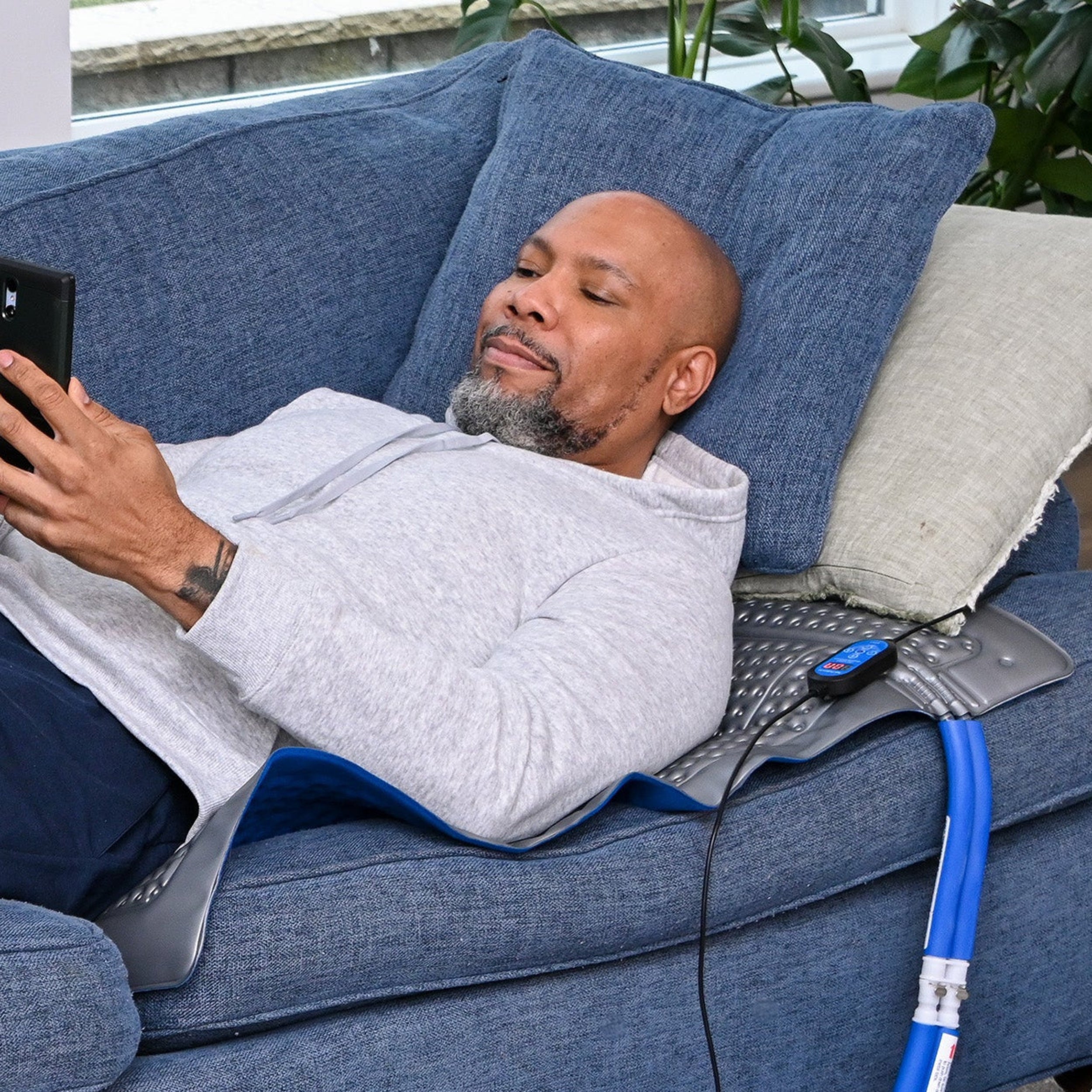 Man sitting on couch using the Polar Active Ice® 3.0 38" x 22" Blanket Cold Therapy Pad attached to the Active Ice® Cold Therapy System