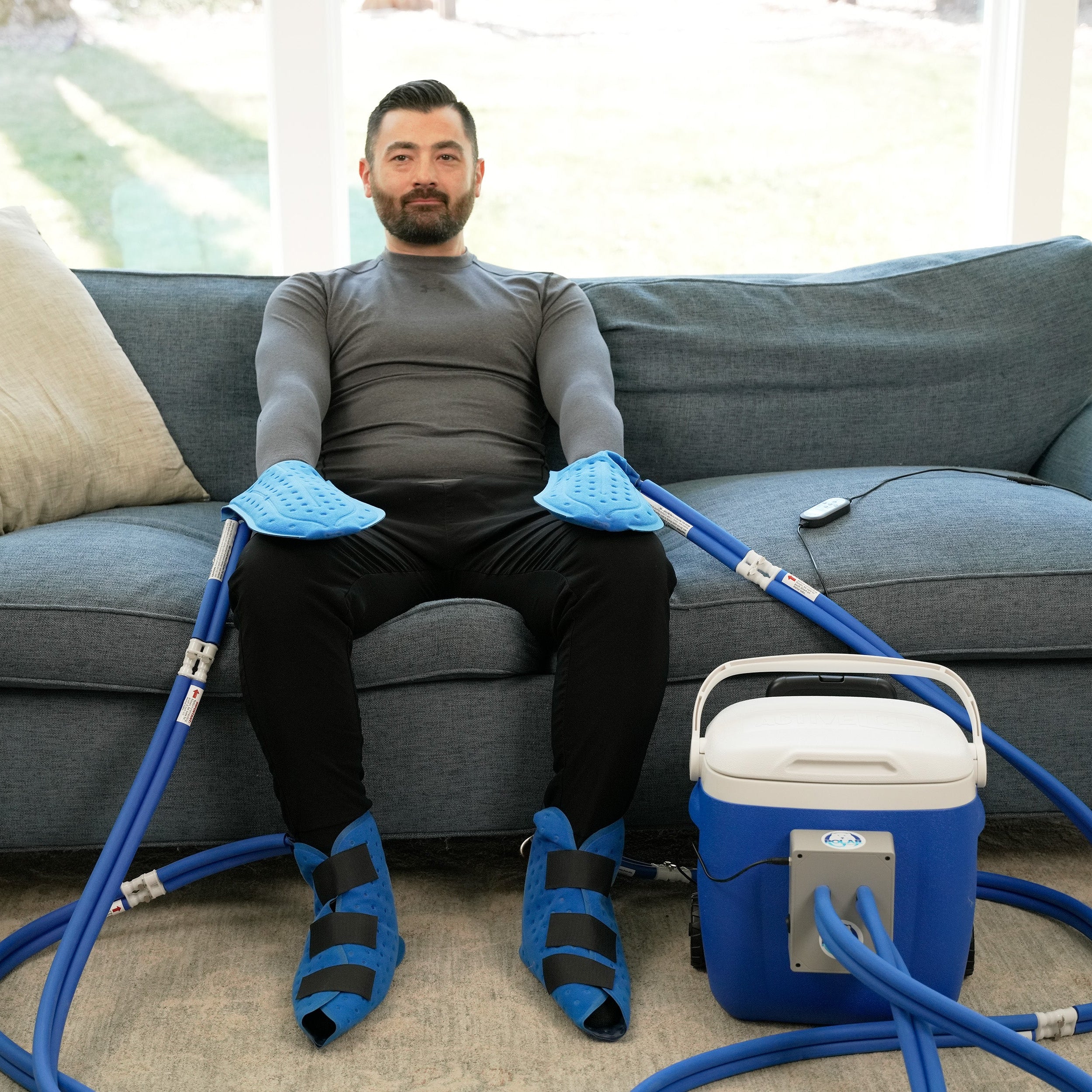 Man sitting on a couch with Active Ice® Extremity Cooling System on his hands and feet in a living room.