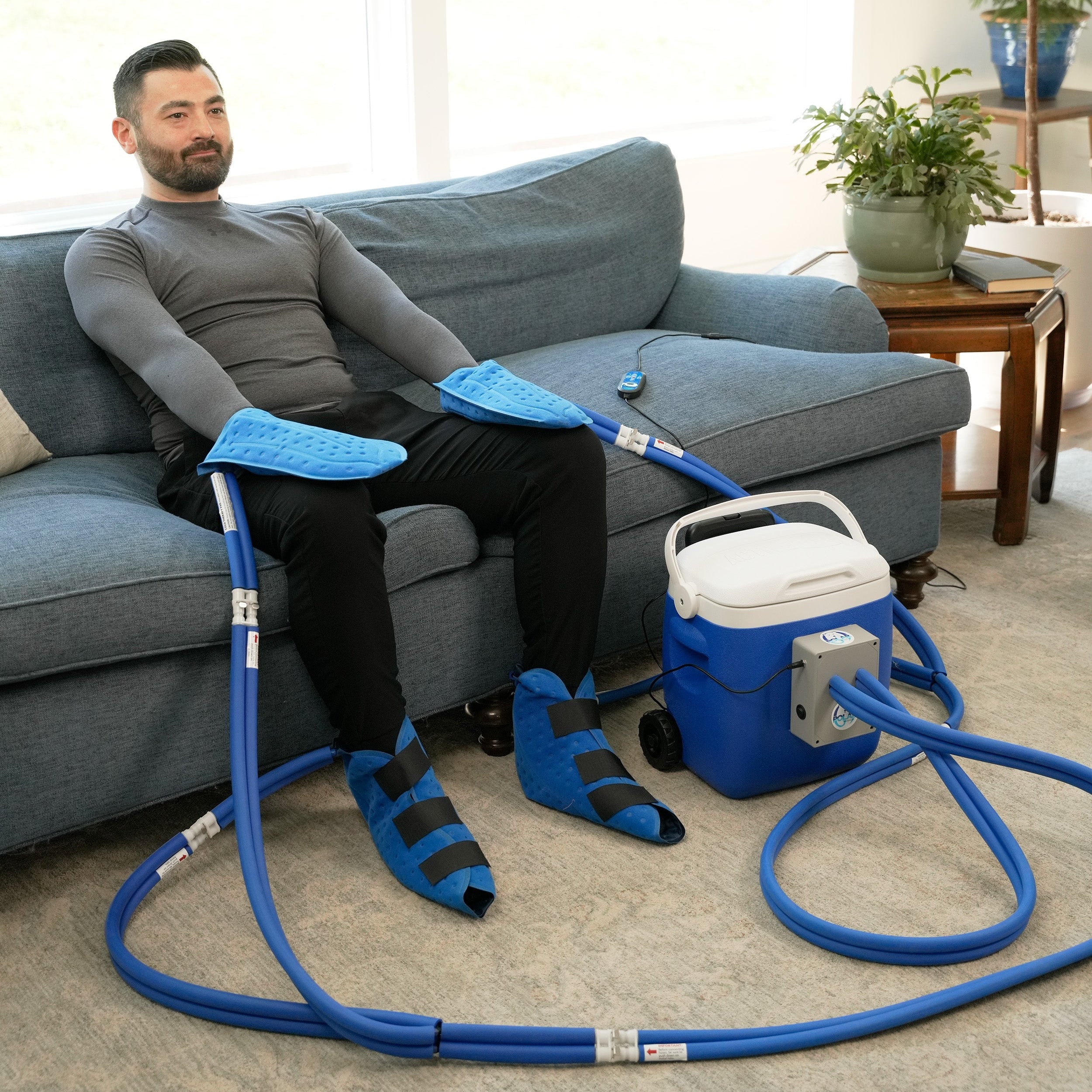 Man sitting on a couch with Active Ice® Extremity Cooling System on his hands and feet in a living room.