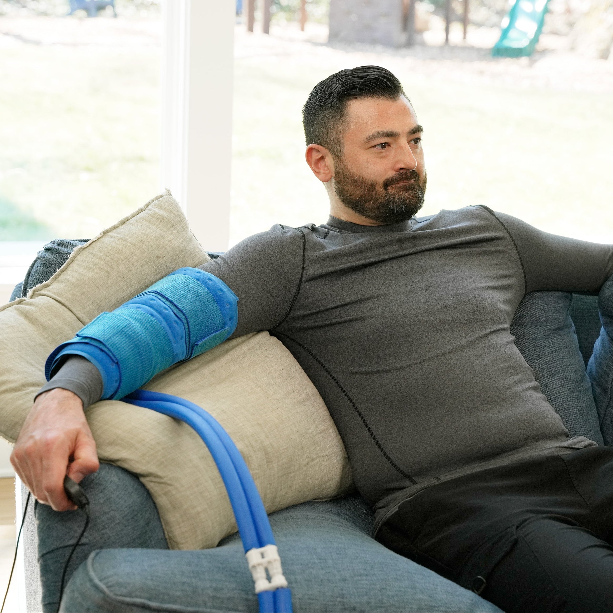 Man sitting on the couch wearing a Universal Rectangular Cold Therapy Pad on his arm.