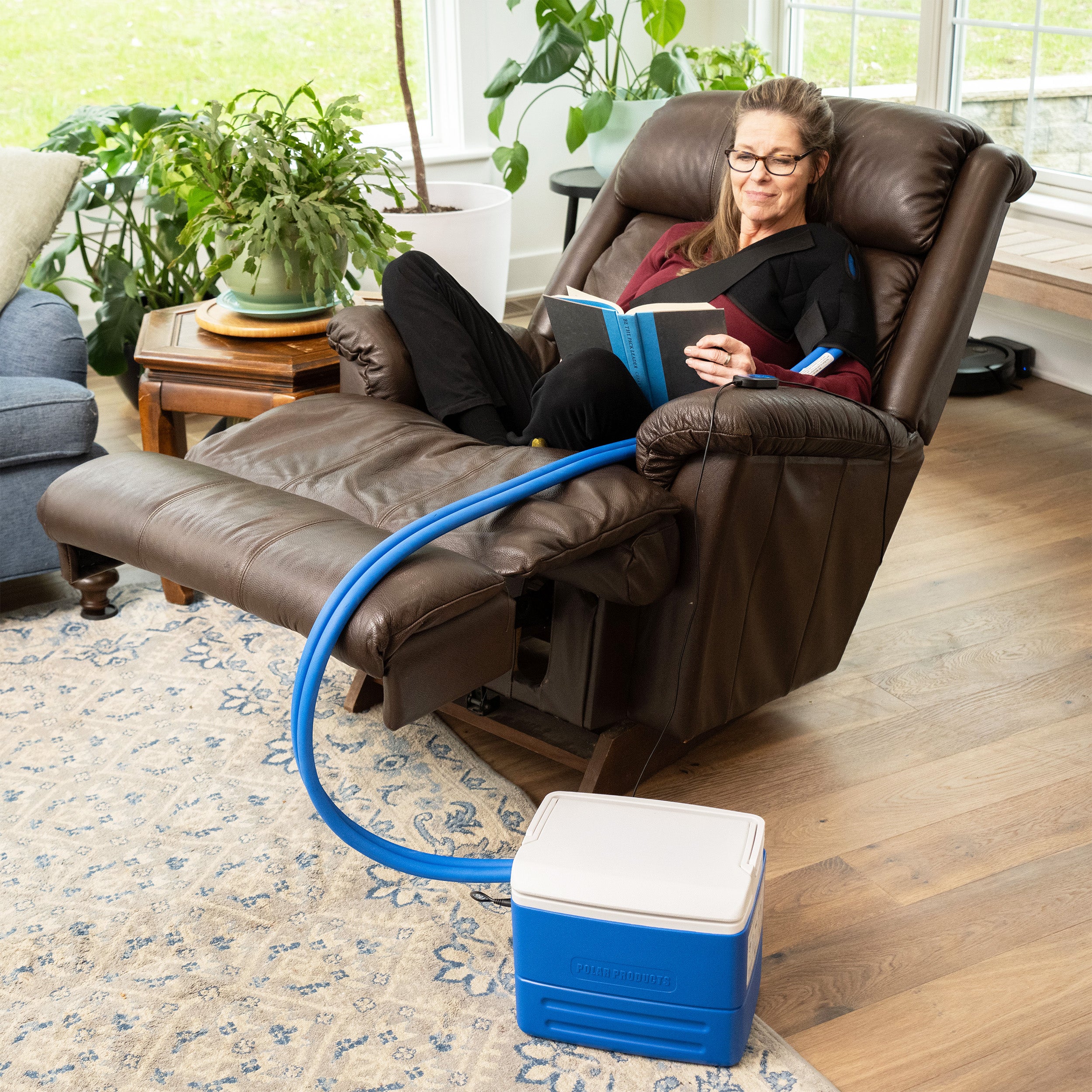 Woman relaxing in recliner chair wearing Active Ice® Targeted Shoulder Cold Therapy System and reading a book