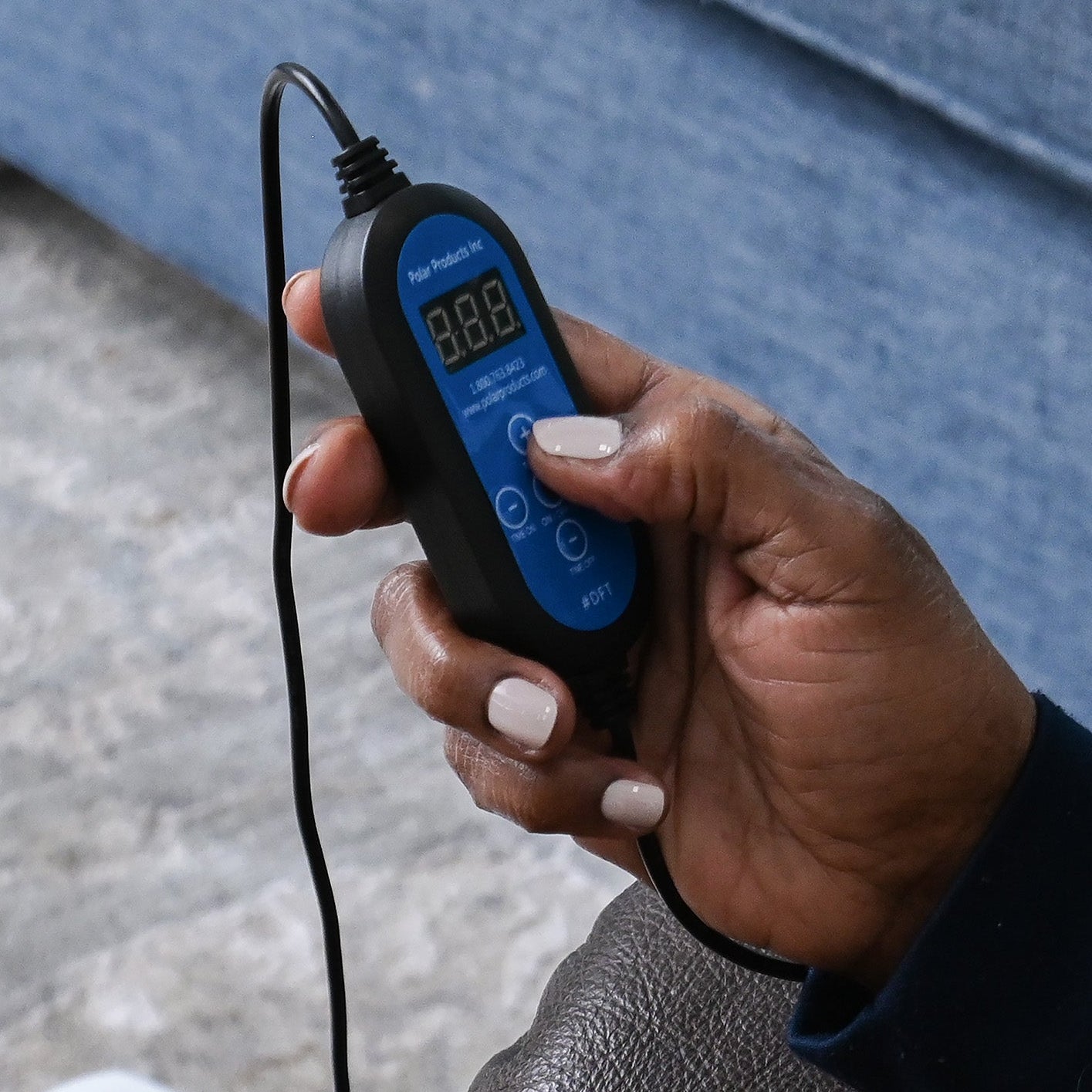 Hand holding a digital timer with a blue display, sitting on a couch.