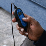Hand holding a digital timer with a blue display, sitting on a couch.