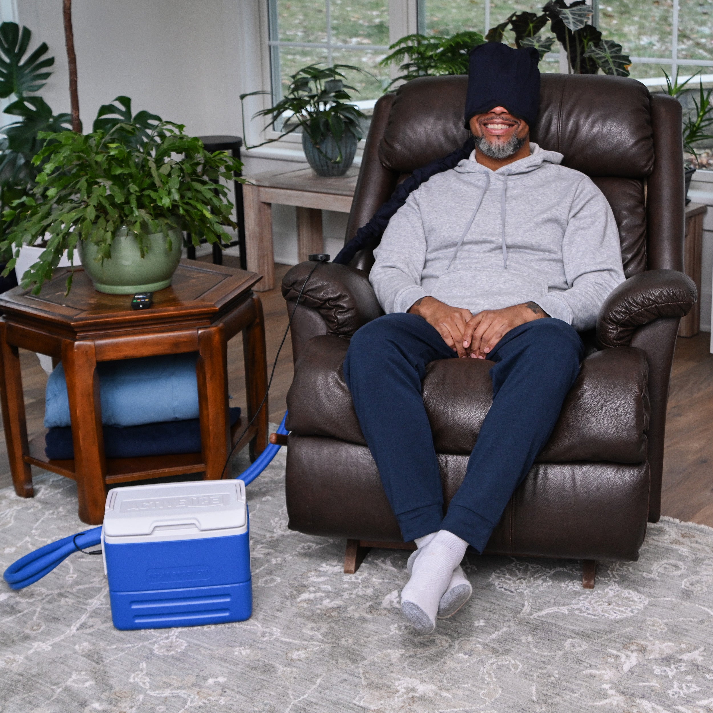 Man sitting on a brown leather recliner wearing the Polar Active Ice® 3.0 Extended Head Cap Cold Therapy System on his head