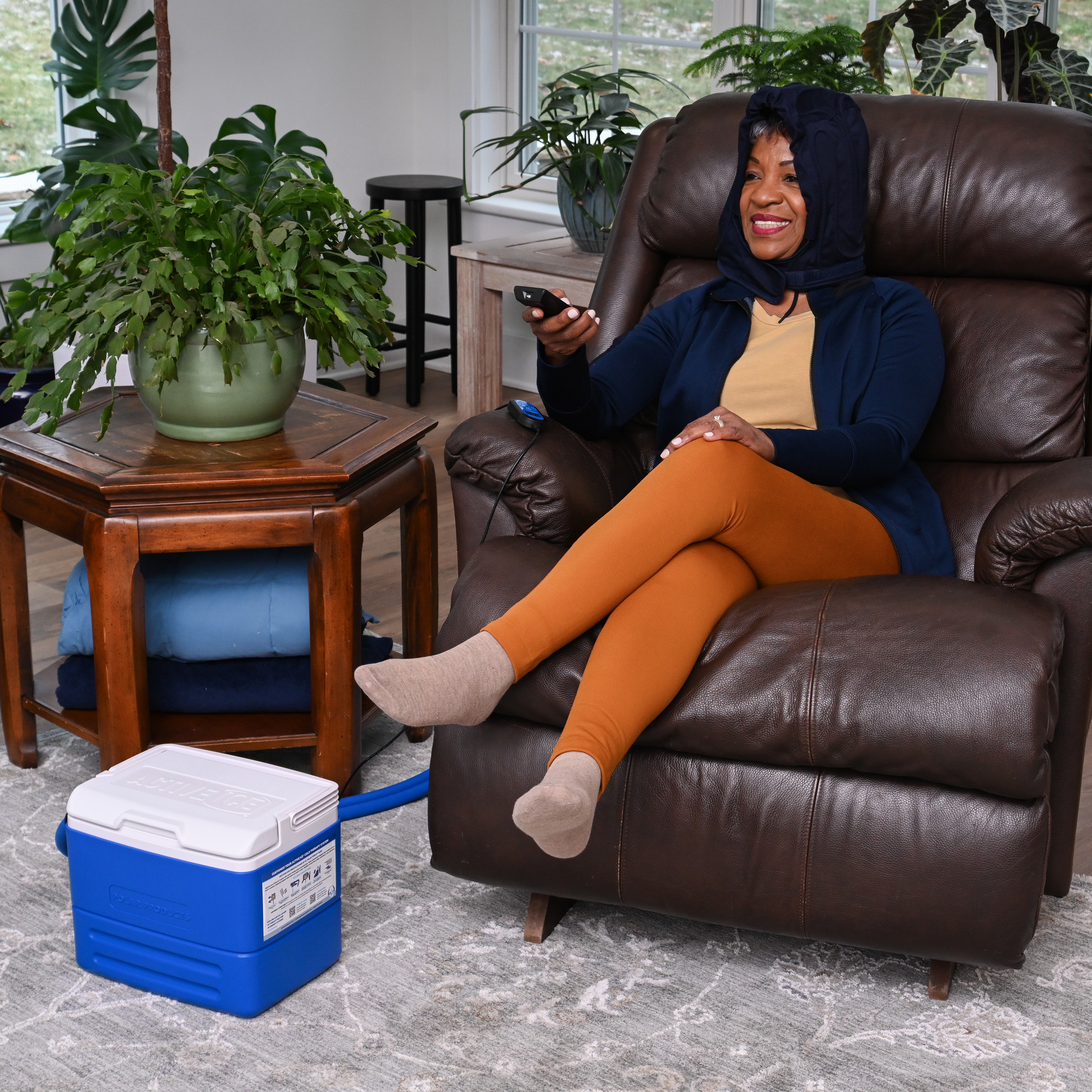 Woman sitting on a brown leather recliner wearing the Polar Active Ice® 3.0 Head Cap Cold Therapy System on her head