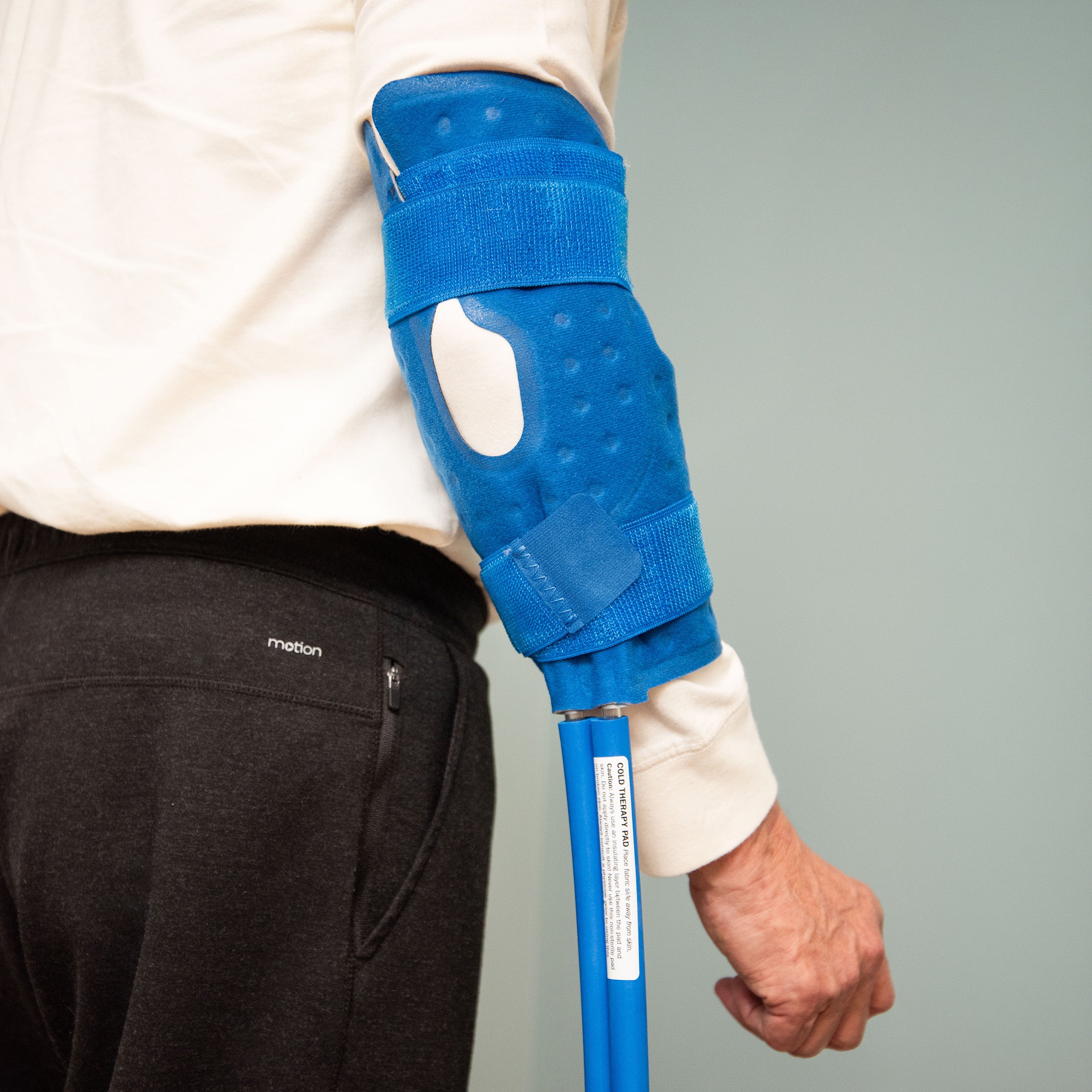 Person with the knee & joint therapy pad for an active ice® cold therapy system on his elbow with a light blue background.