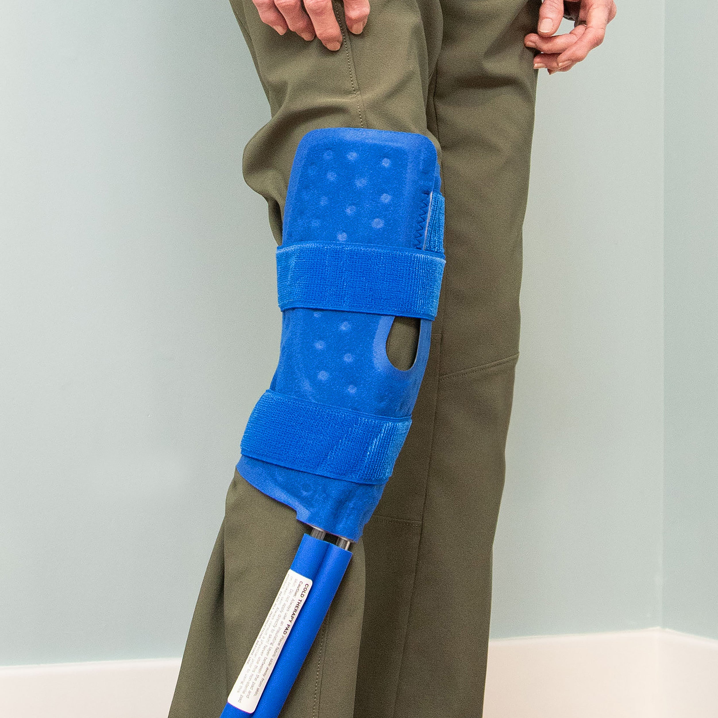 Blue Knee & Joint therapy pad wrapped around someone's knee on light background.