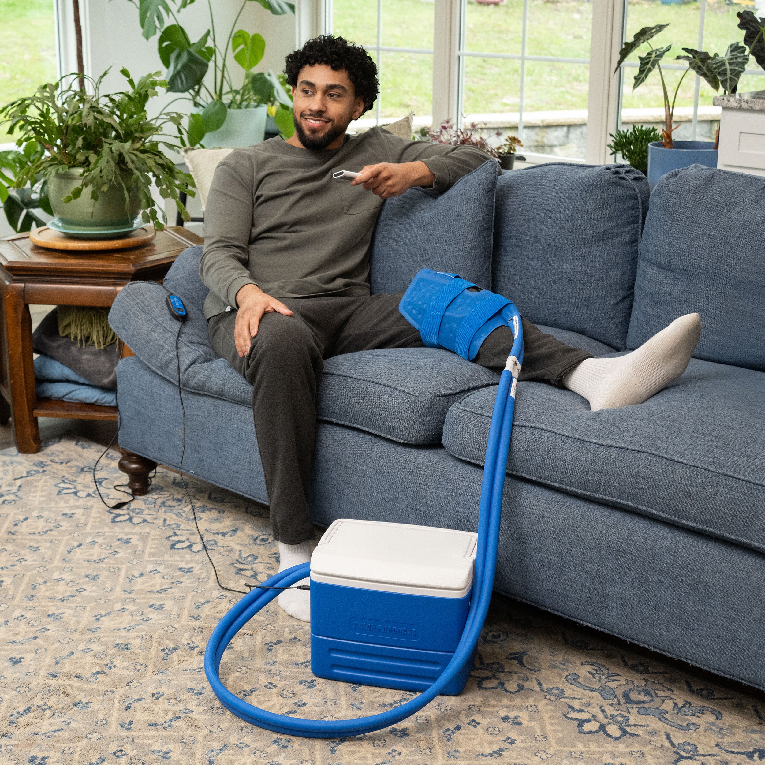 Man relaxing on a blue couch using the Polar Active Ice® knee & joint system on his knee in a living room setting