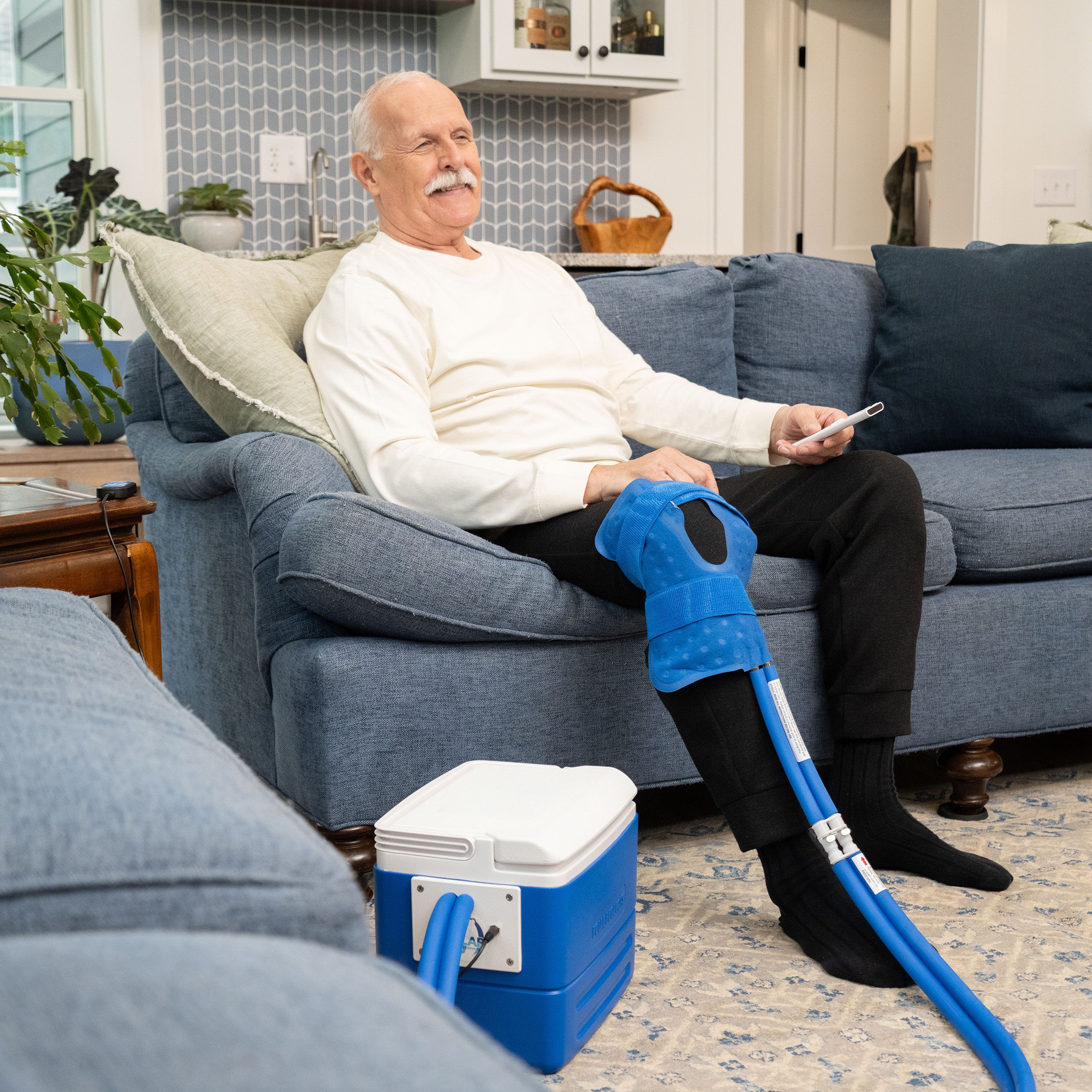 Man sitting on couch holding remote and using the Active Ice® Knee & Joint Cold Therapy System