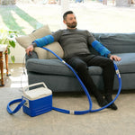 Man sitting on a couch using the Double Universal Rectangular Cold Therapy System on both of his arm in a living room setting
