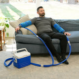 Man sitting on a couch using the Double Universal Rectangular Cold Therapy System on both of his arm in a living room setting