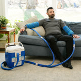 Man sitting on a couch using the Double Universal Rectangular Cold Therapy System on both of his arms in a living room setting