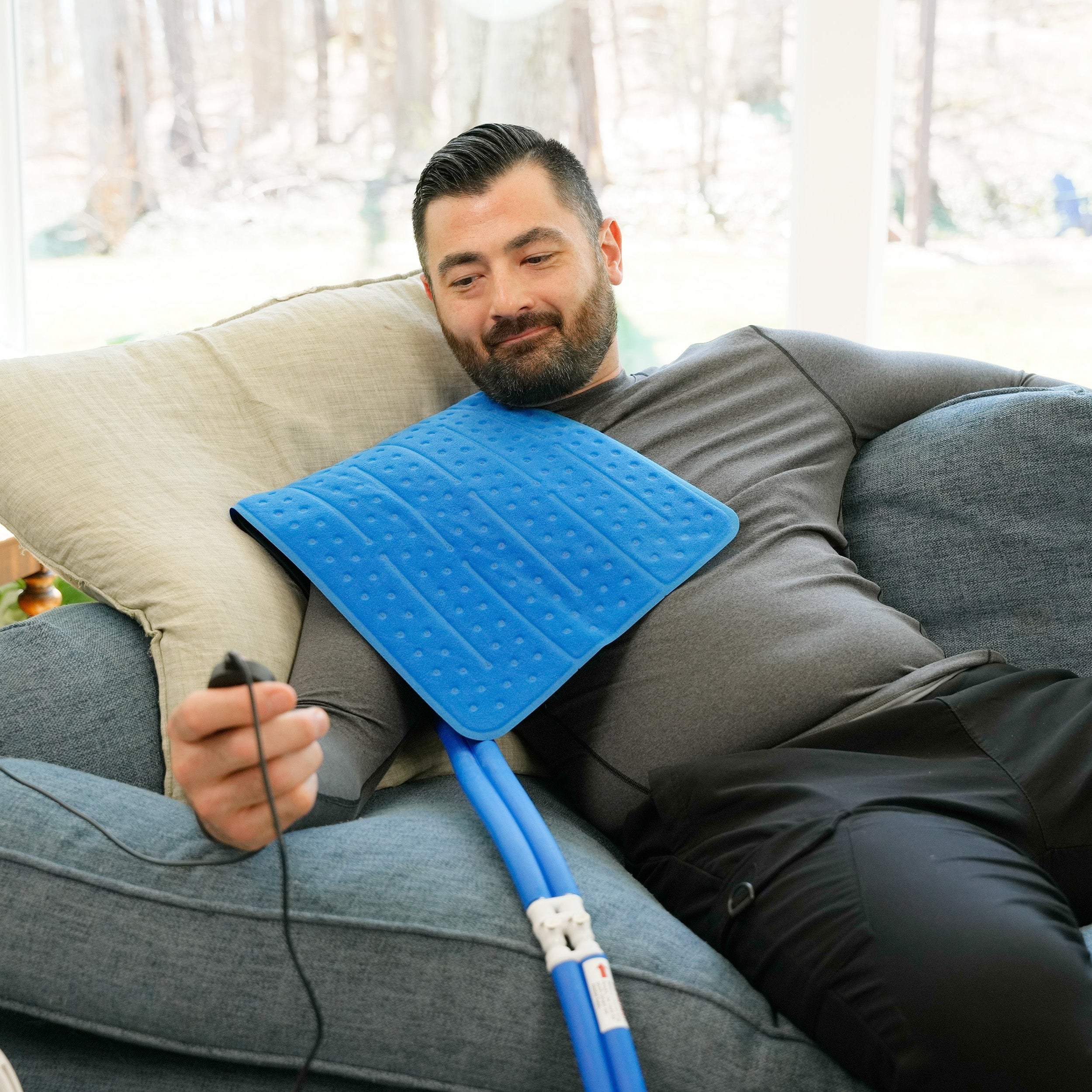 Man sitting on a couch using the Universal Rectangular Cold Therapy System on his shoulder in a living room setting