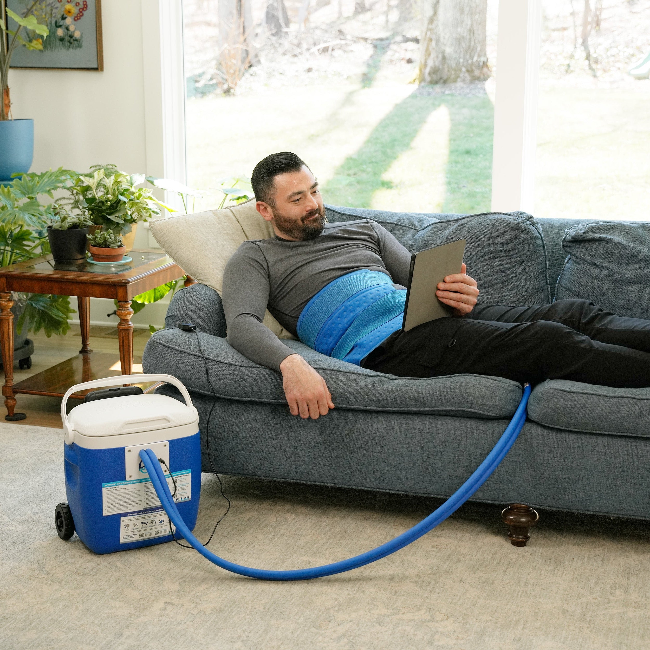 Man sitting on a couch using the Universal Rectangular Cold Therapy System on his hip in a living room setting