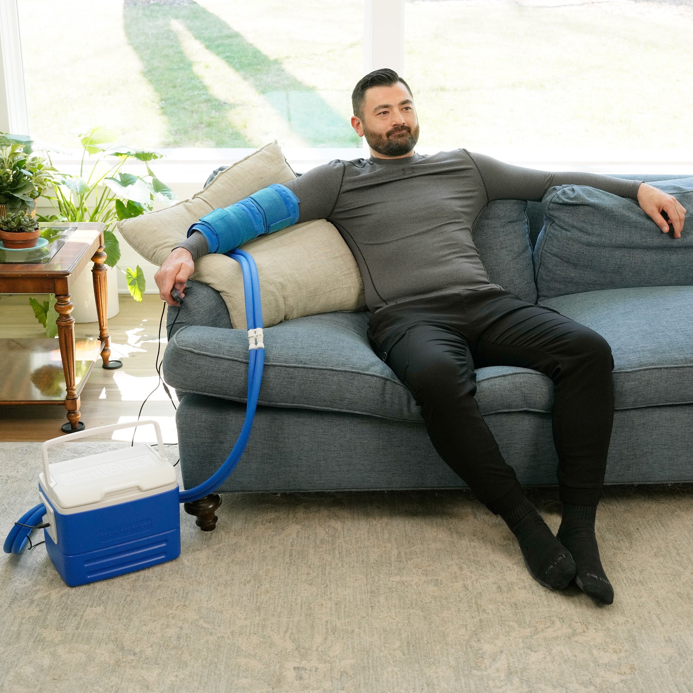 Man sitting on a couch using the Universal Rectangular Cold Therapy System on his arm in a living room setting
