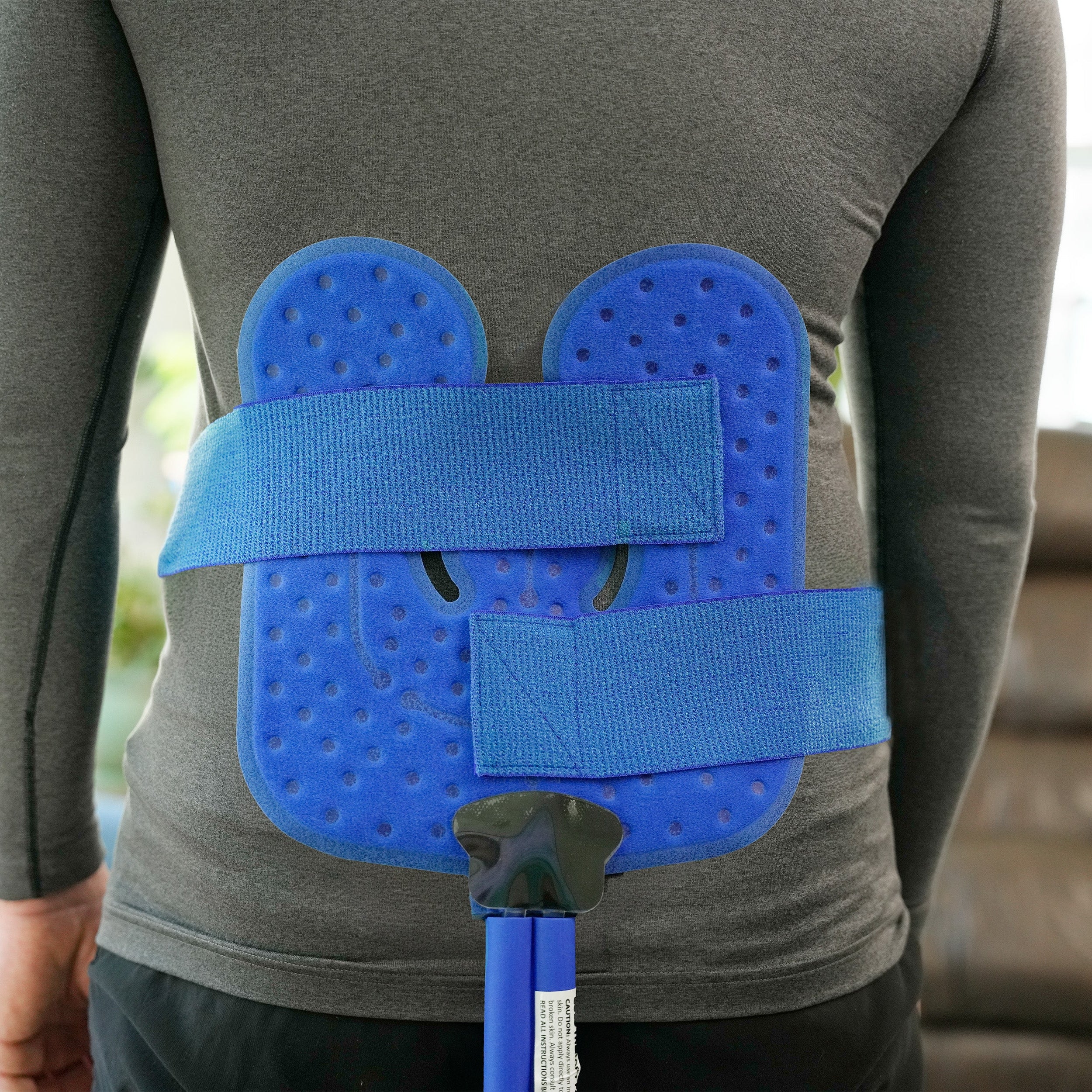 Man wearing a Universal Cold Therapy Pad on his lower back in a blurred living room setting.