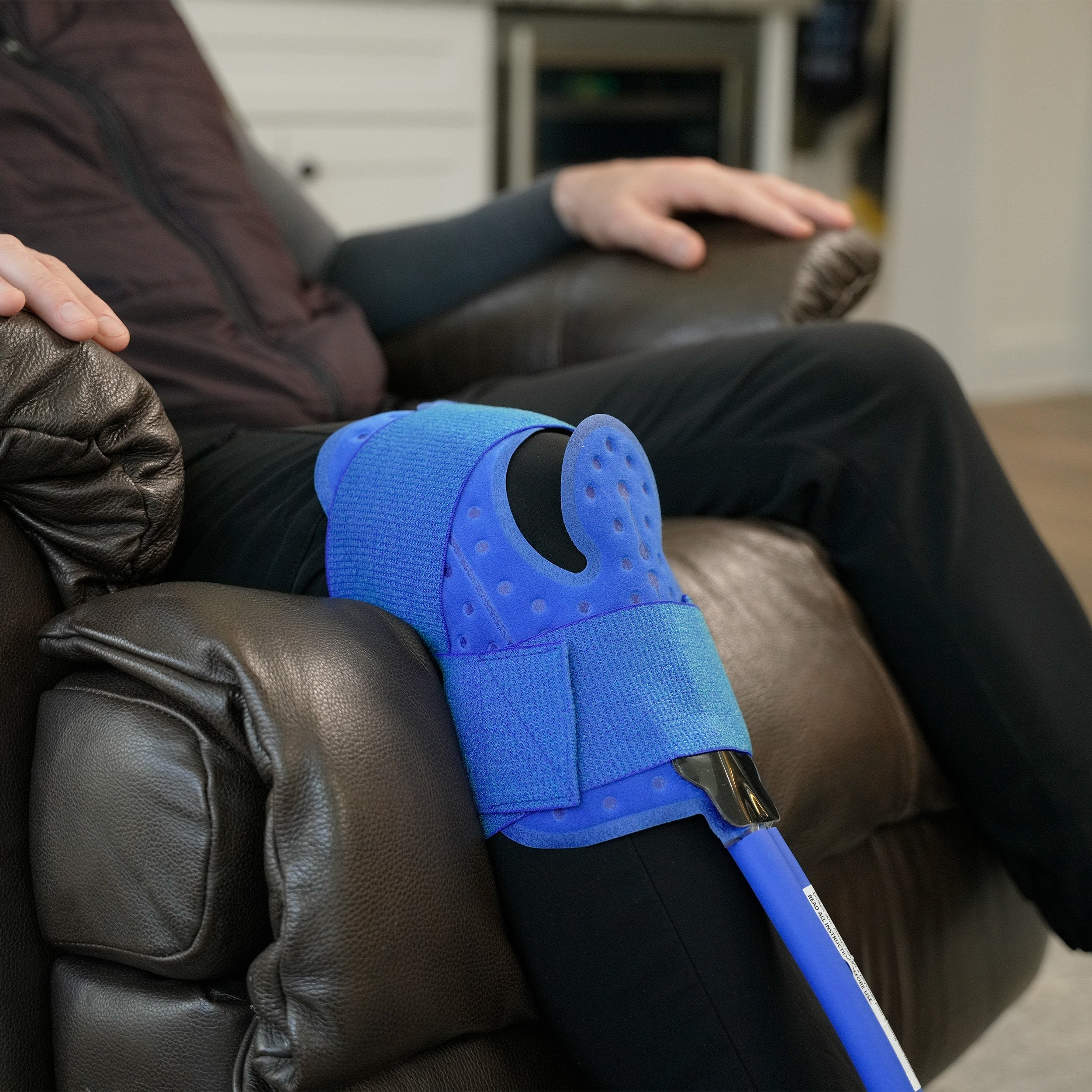 Universal Cold Therapy Pad on a man's knee who is sitting in a brown recliner in a home setting.