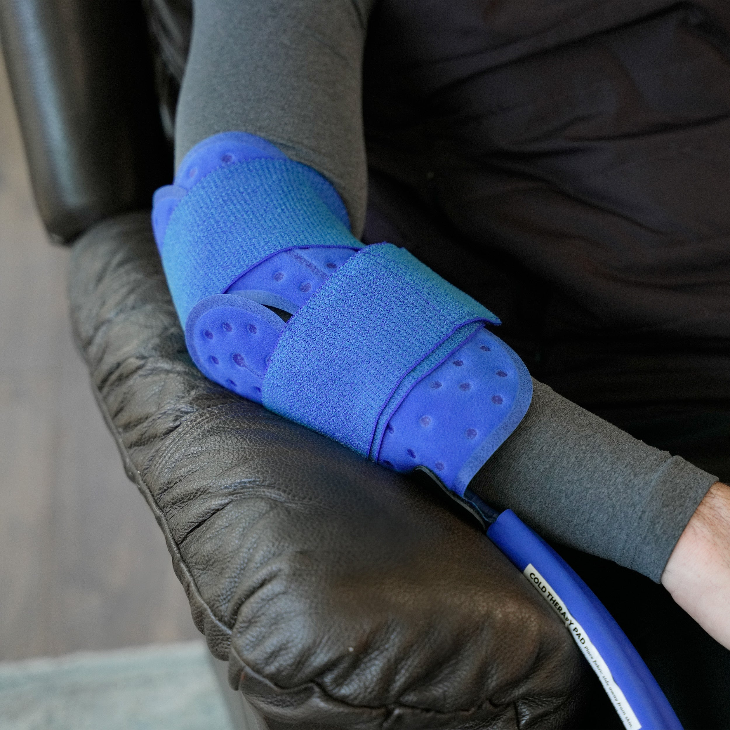 Universal Cold Therapy Pad on a man's elbow who is sitting in a brown recliner in a living room setting.