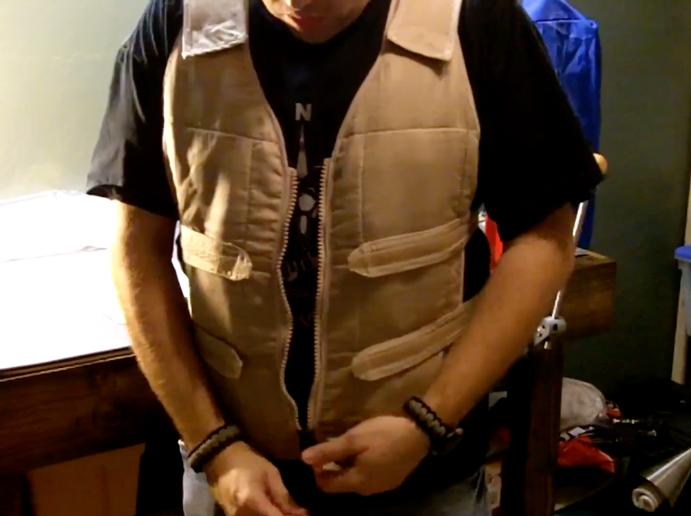 A person wearing a beige adjustable cooling vest over a black t-shirt, standing in a room.