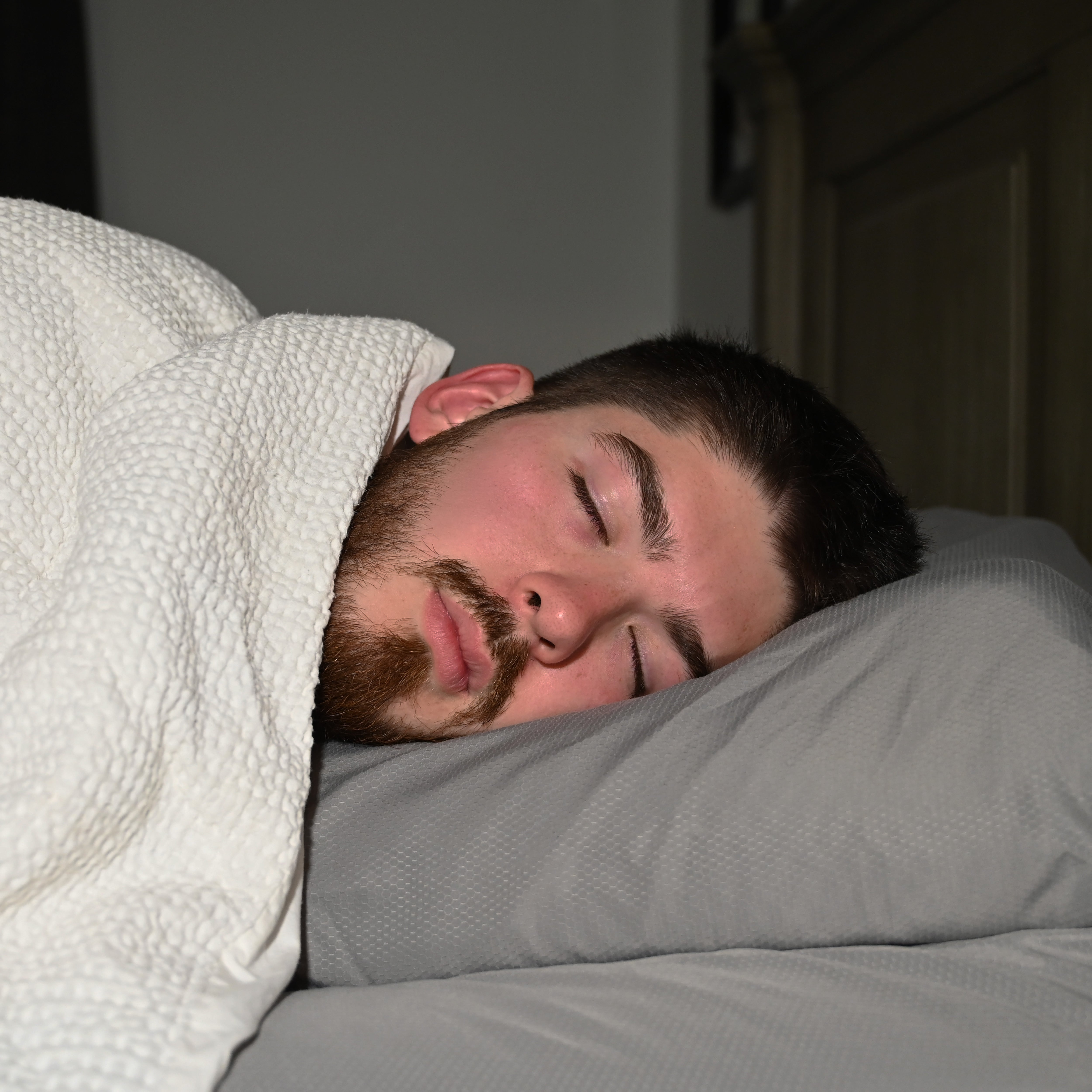 Man sleeping under a white blanket on a pillow with a dark background