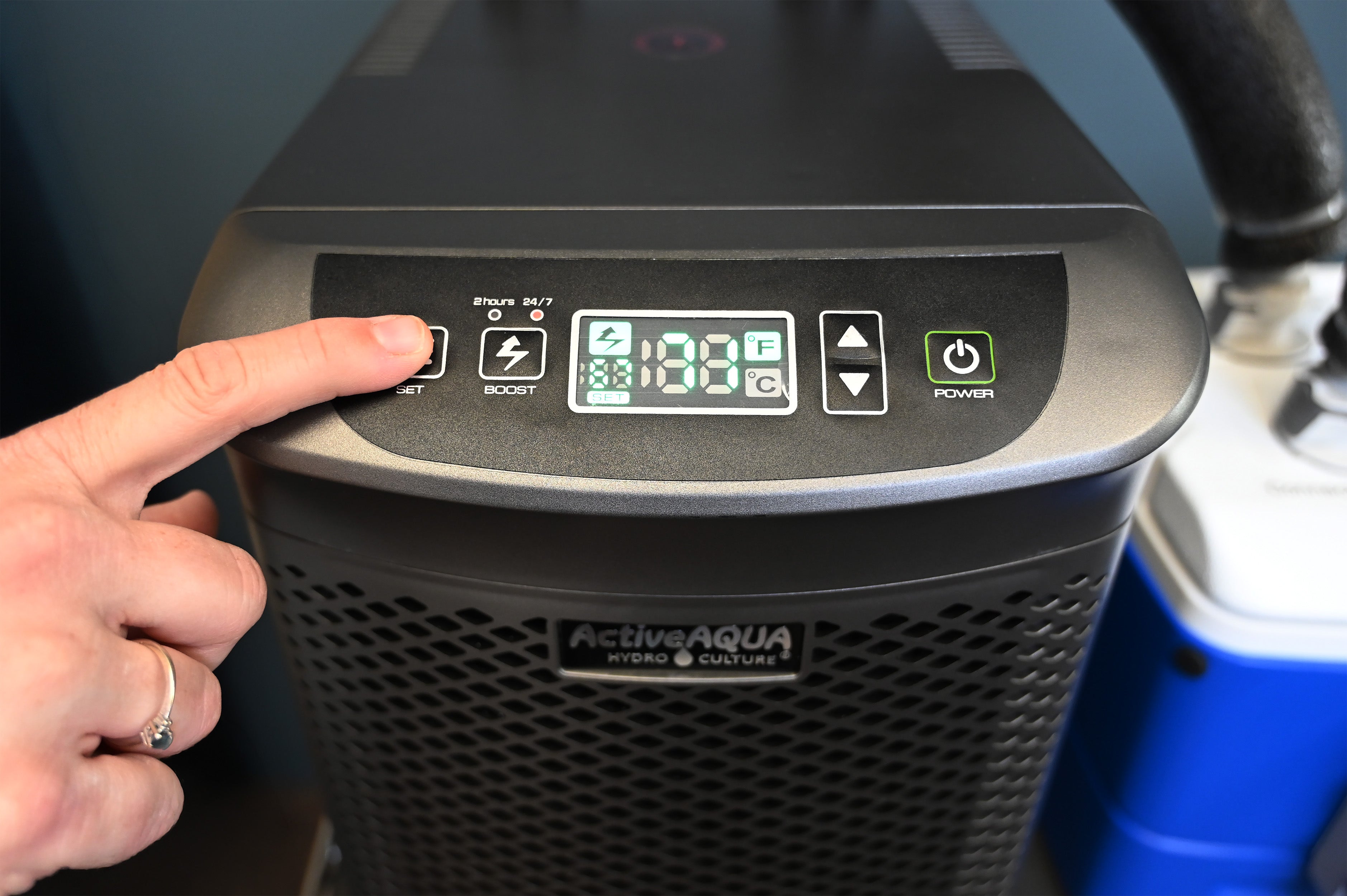 A close-up of a person's hand pressing the power button on the control panel of an Arctic Chiller, with a blue and white container visible in the background.