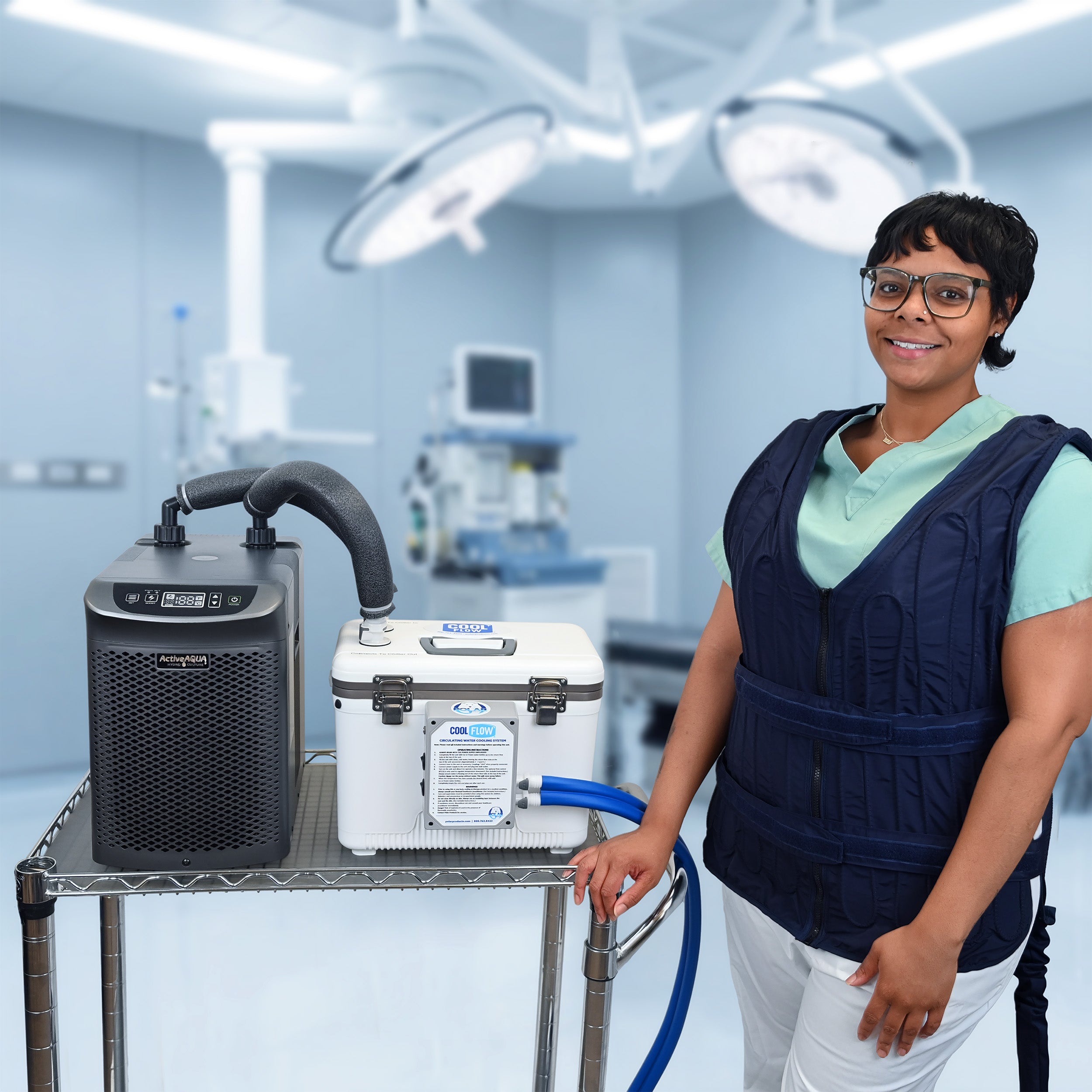 A woman in medical scrubs stands beside a metal cart holding an Arctic Chiller and 13-quart cooling reservoir in a bright operating room. She's attached to the reservoir with the fitted circulating cooling vest. The background shows surgical lights and medical equipment.