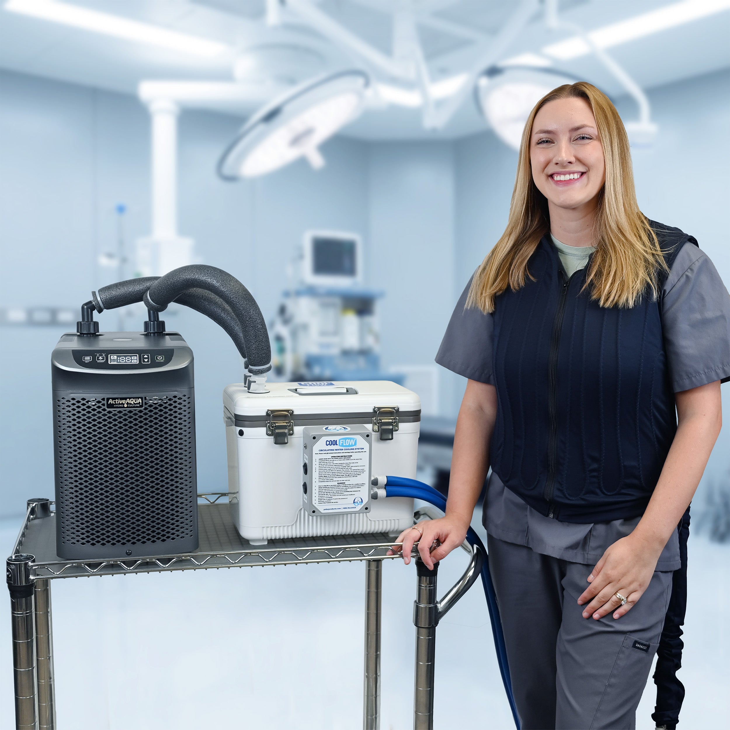 A woman in medical scrubs stands beside a metal cart holding an Arctic Chiller and 13-quart cooling reservoir in a bright operating room. She's attached to the reservoir with the fitted circulating cooling vest. The background shows surgical lights and medical equipment.
