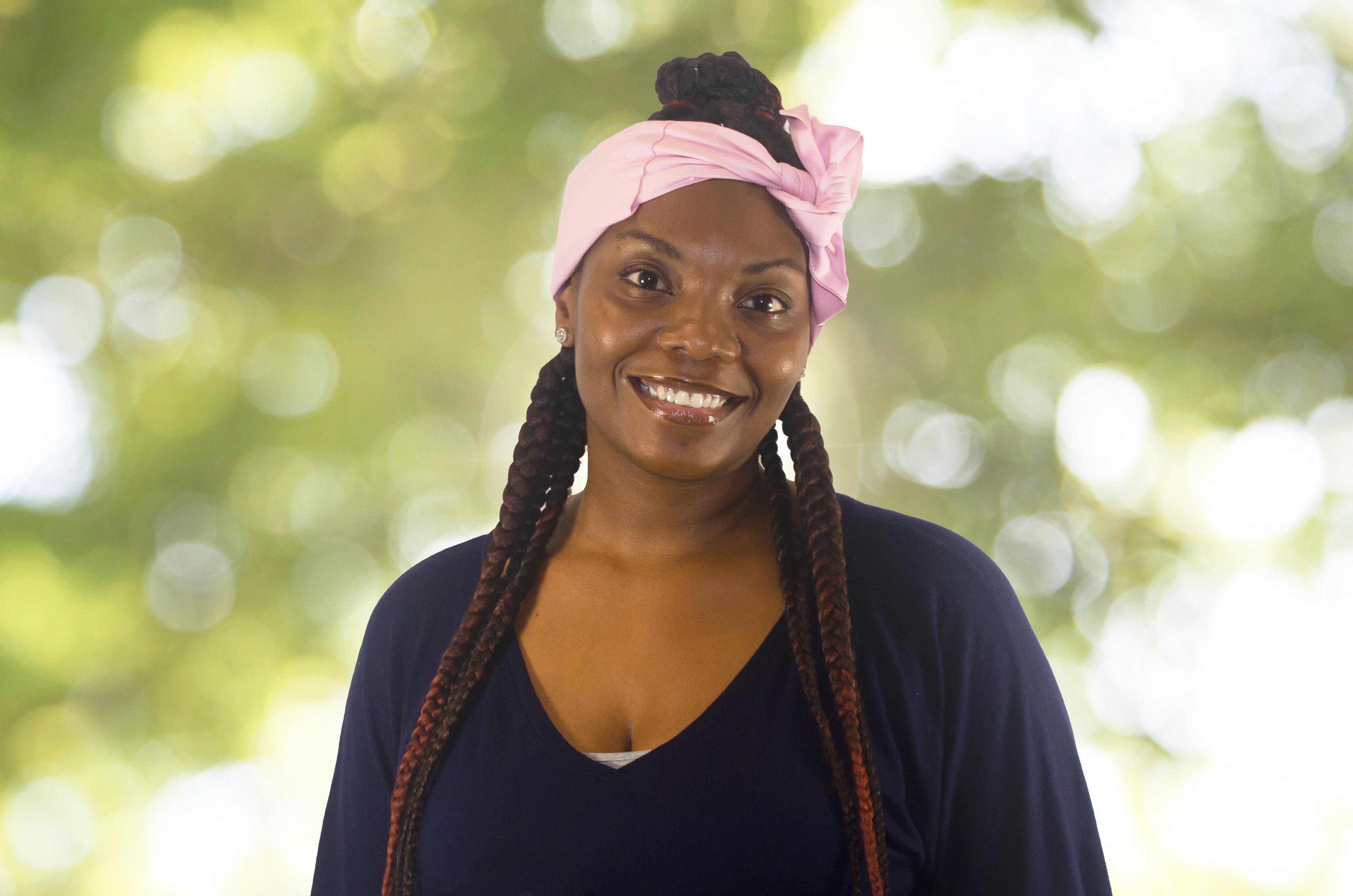 Woman with braided hair wearing a pink headscarf against a blurred green background