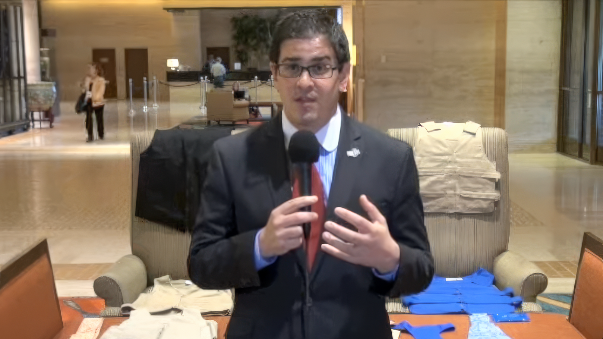 Man in a suit speaking into a microphone in a lobby setting