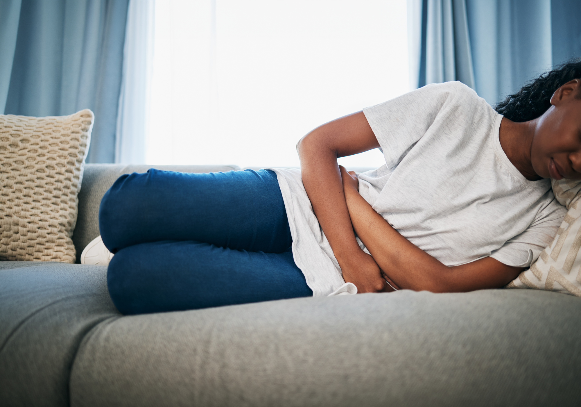Person lying on a couch with a pillow under their head, possibly experiencing discomfort.