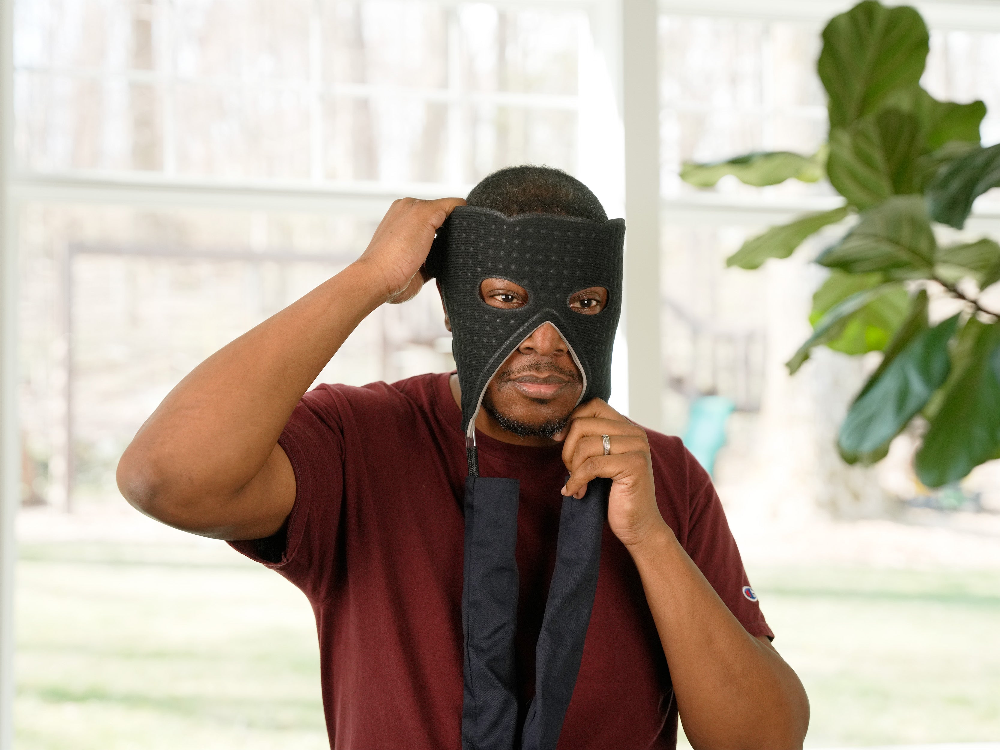 Man applying Face Cold Therapy Pad to his head in an indoor setting with plants