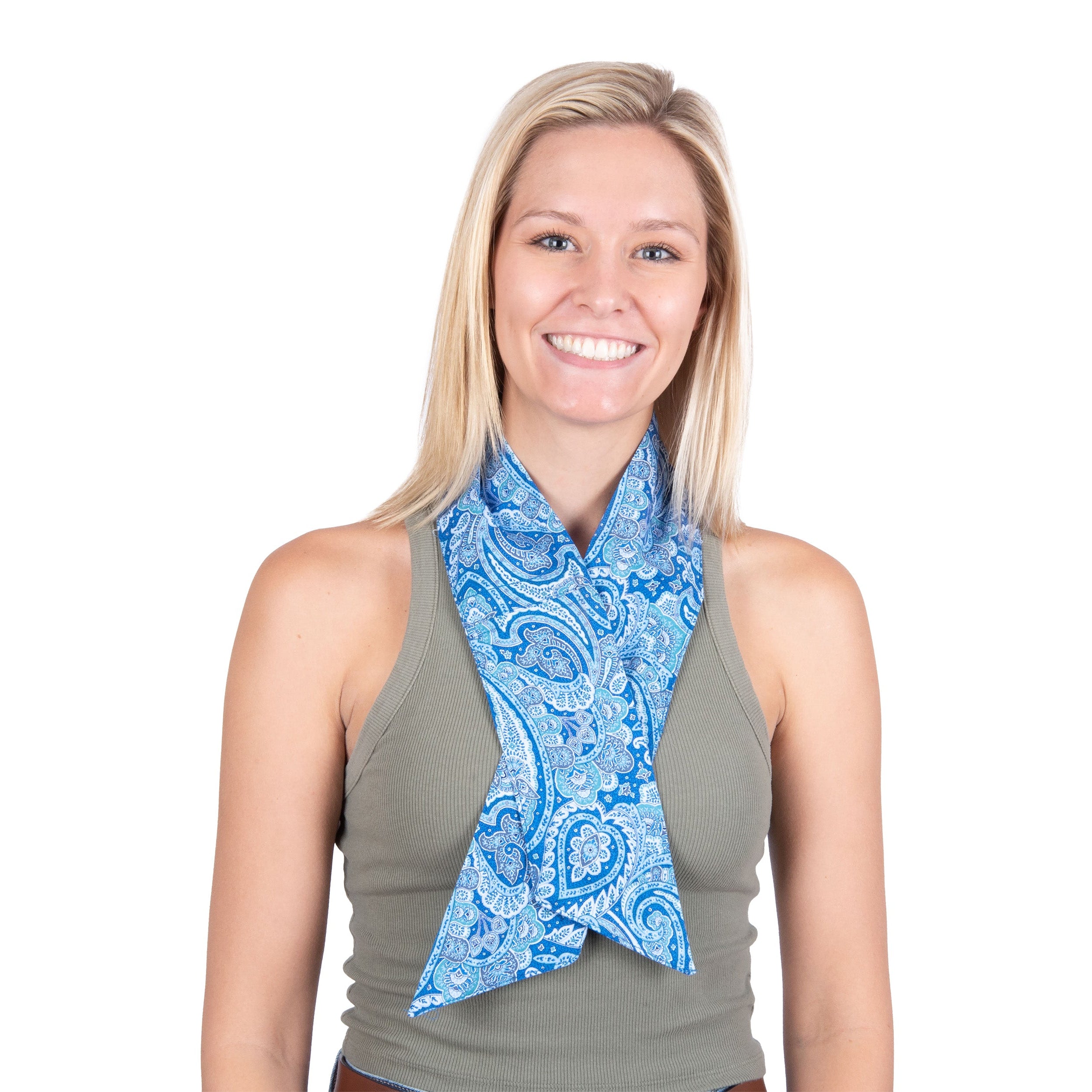 A smiling blonde woman wearing a blue and white paisley patterned cooling fashion neck scarf tied around her neck over a gray sleeveless top, isolated on a white background.
