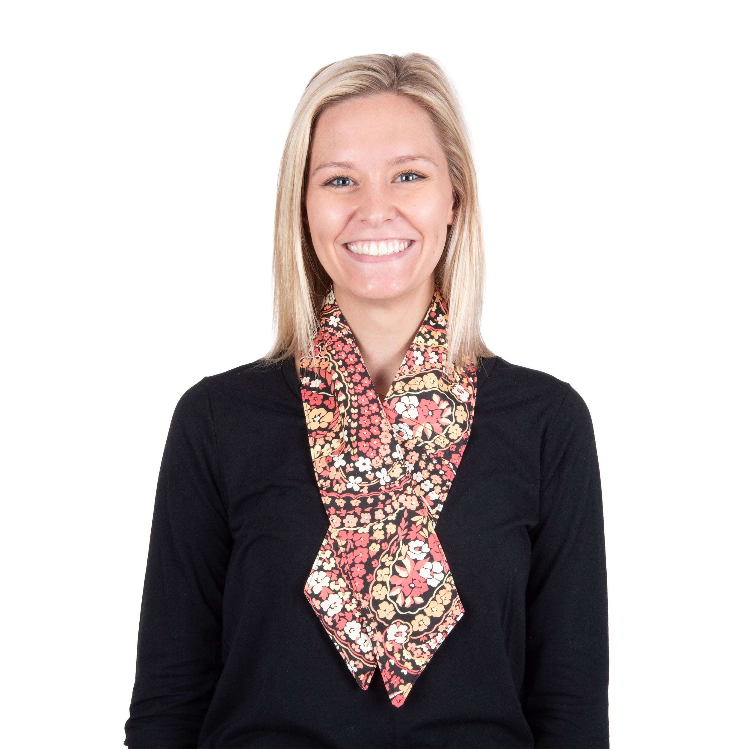 A smiling blonde woman wearing a black long-sleeve top and cooling fashion neck scarf with a floral and paisley design in pink, red, beige, and black, shot against a solid white background.