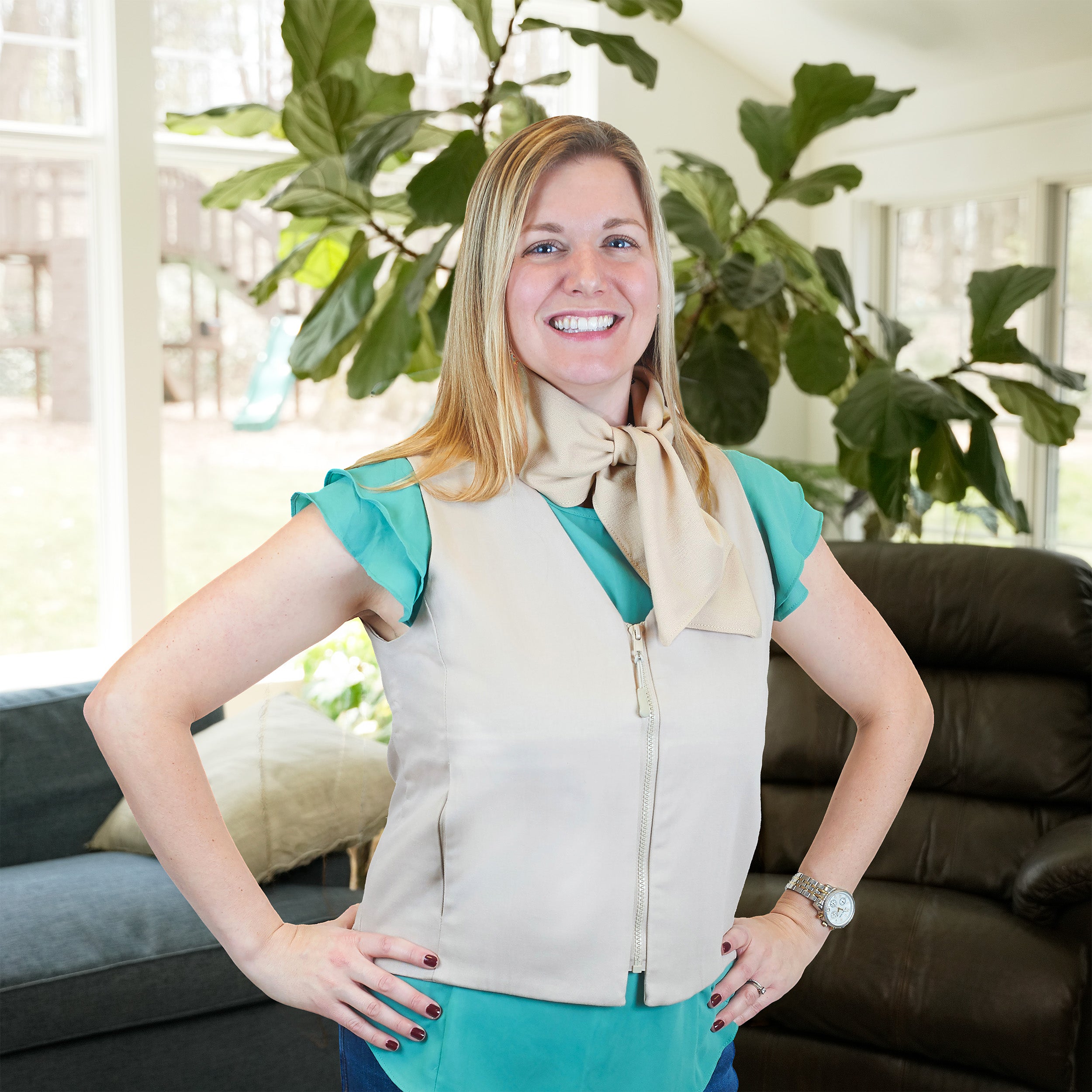 Woman wearing a beige cooling fashion vest with teal sleeves and a beige cooling neck scarf, standing in a living room.