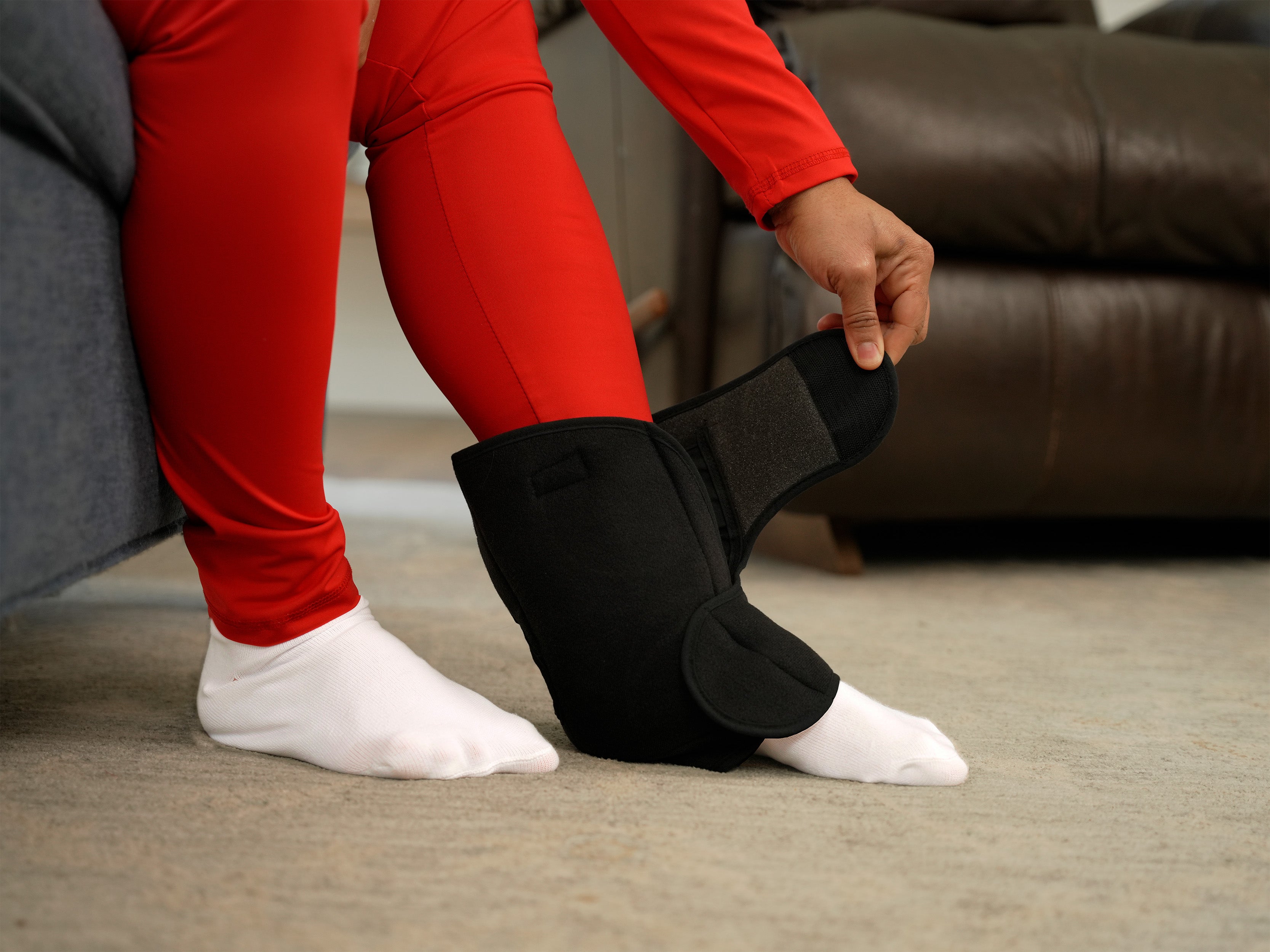 Person wearing a black Soft Ice® Ankle Wrap on a carpeted floor.