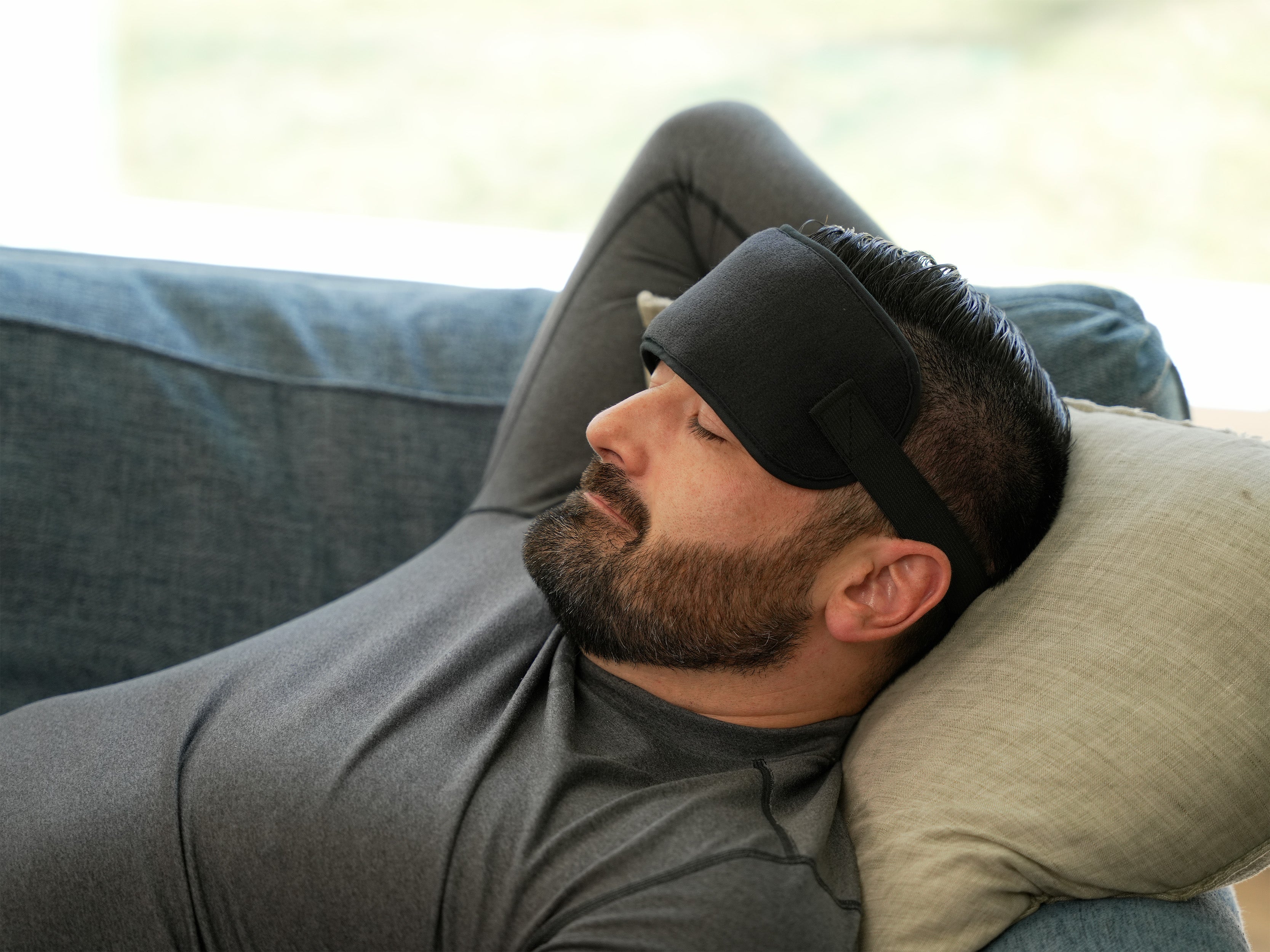 Man wearing a Soft Ice® Head Wrap and resting on a pillow in a living room.