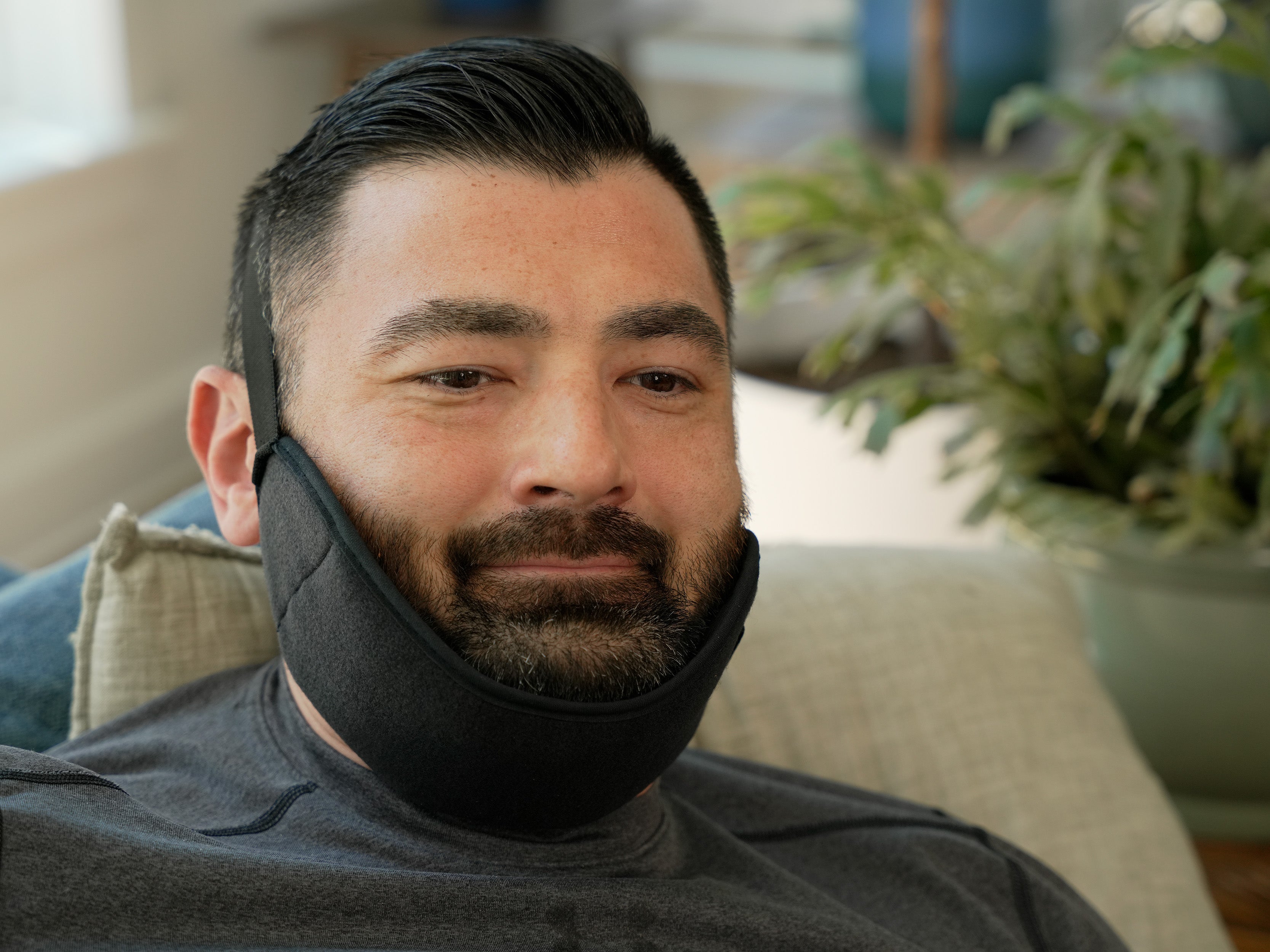 Man wearing a black Soft Ice® Jaw Wrap in a home setting with plants in the background