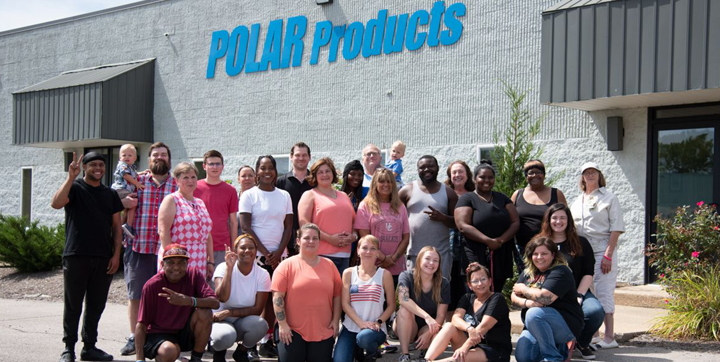 A large group of people posing for a group photo in front of a building with 'POLAR Products' written in blue text on the wall.