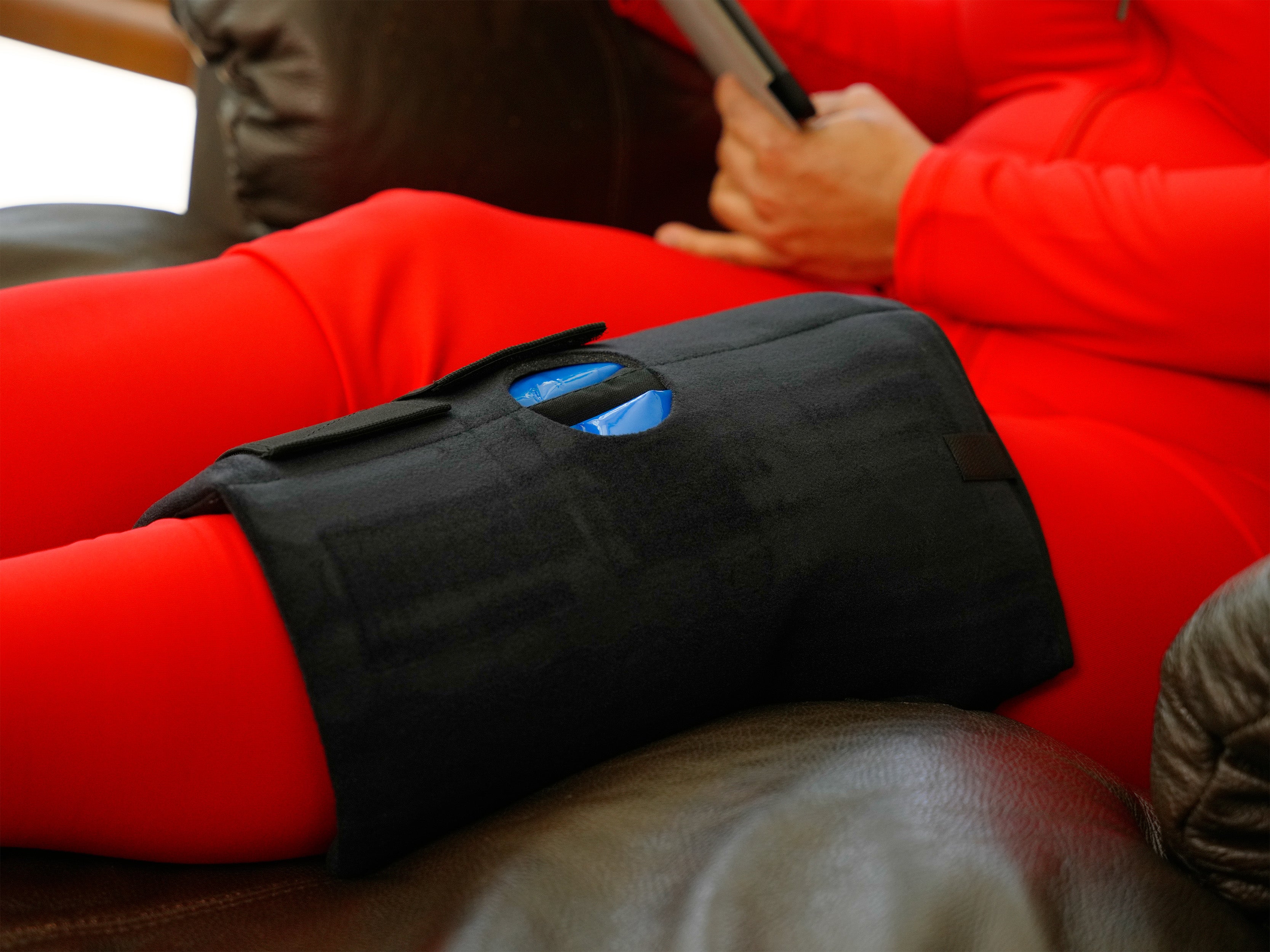 Person wearing a black Soft Ice® Knee Wrap on a brown leather recliner.