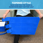 A person seated in an armchair holds a bright blue tapered full circumference knee cold therapy pad, with text at the top reading 'TAPERED STYLE' and 'WIDE END FOR THE THIGH & NARROWER END FOR THE CALF.'.