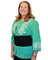 Woman wearing a green blouse with white embroidery and a black cooling torso wrap on a white background