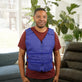Man wearing a blue Kool Max® Adjustable Zipper Cooling Vest in a bright living room with plants in the background.