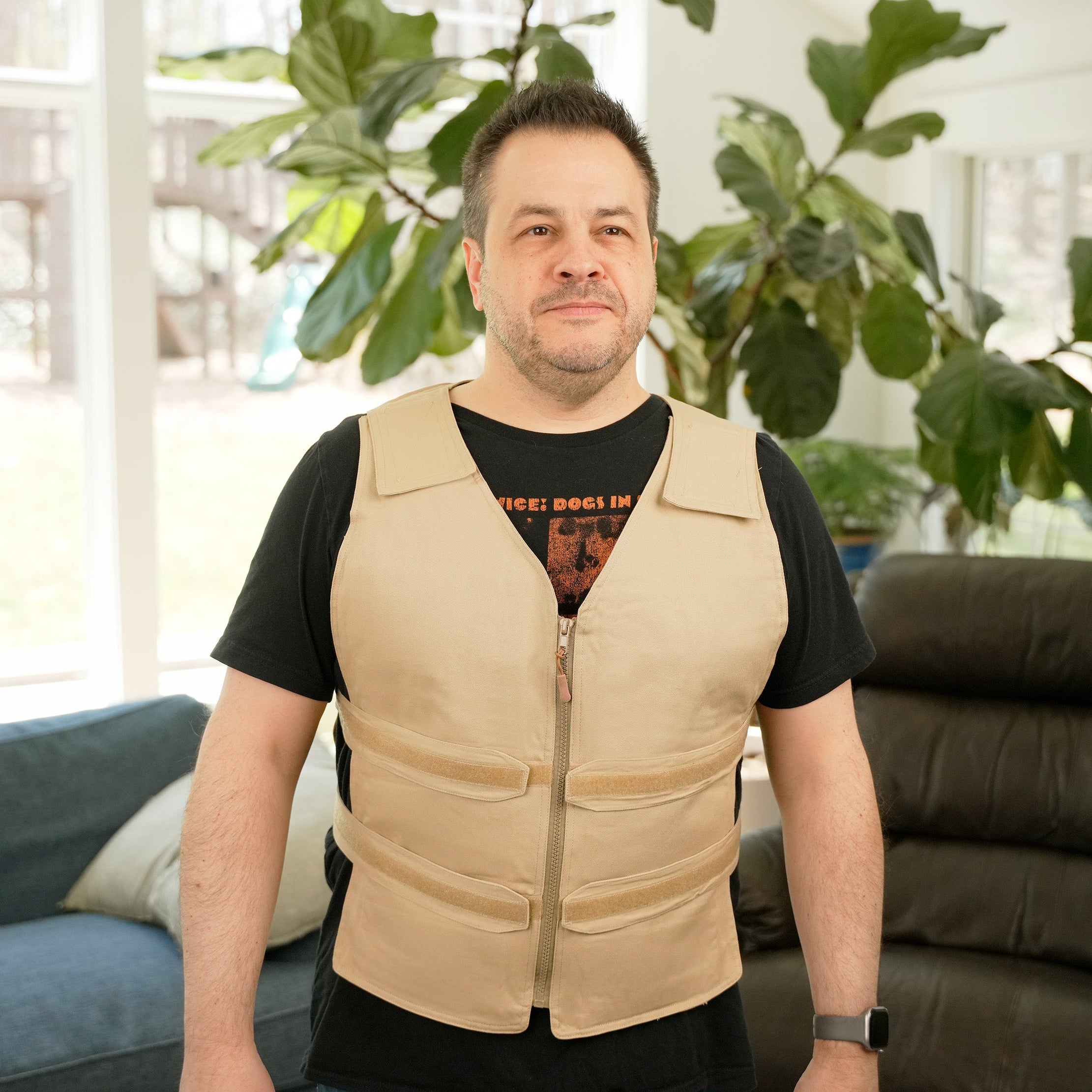 Man wearing a khaki Adjustable Zipper Cooling Vest with Cool58® Packs in a bright living room with plants in the background.
