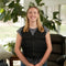 Woman wearing a black Adjustable Zipper Cooling Vest with Kool Max® Packs in a bright living room with plants.