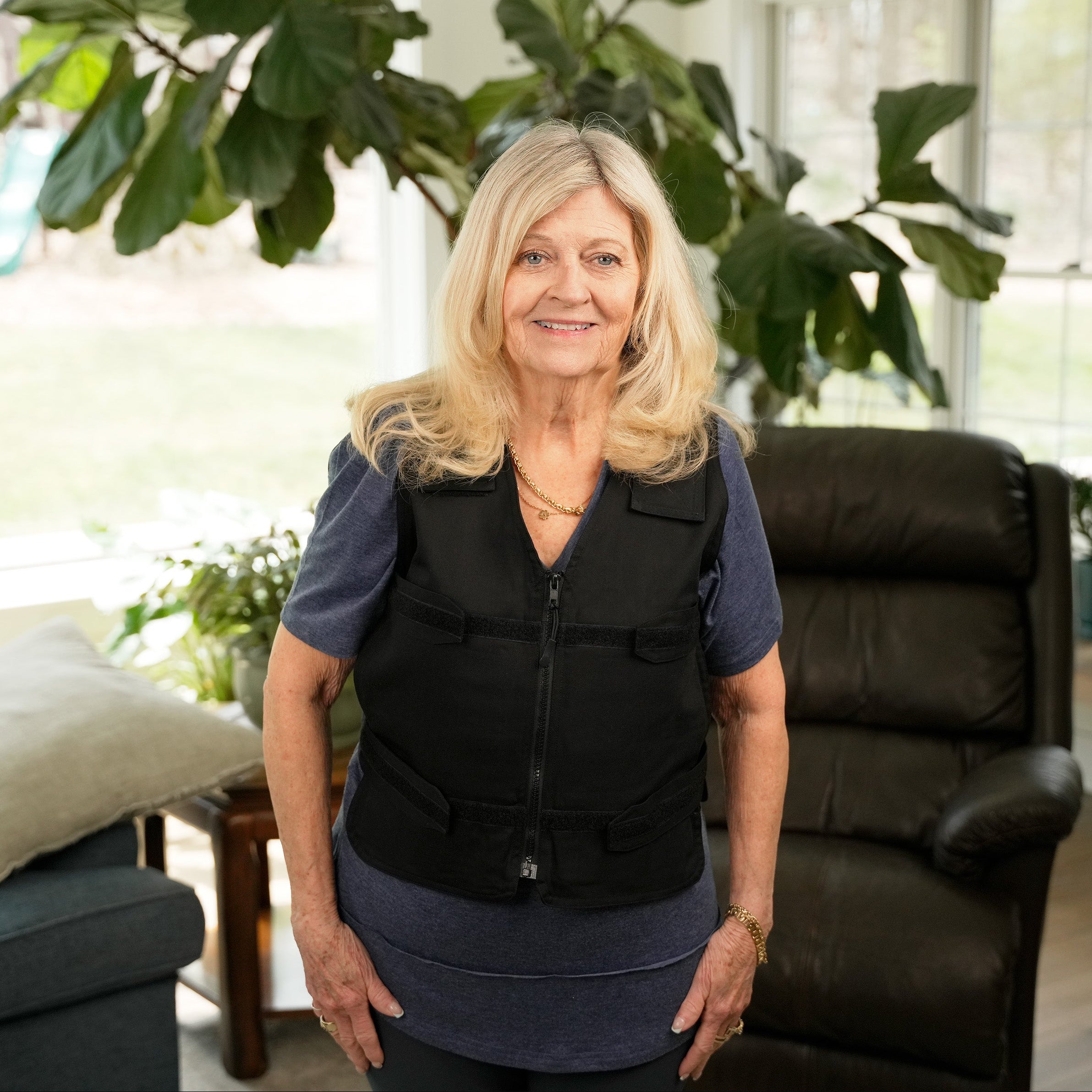 Woman wearing a black Adjustable Zipper Cooling Vest with Cool58® Packs in a bright living room with plants.