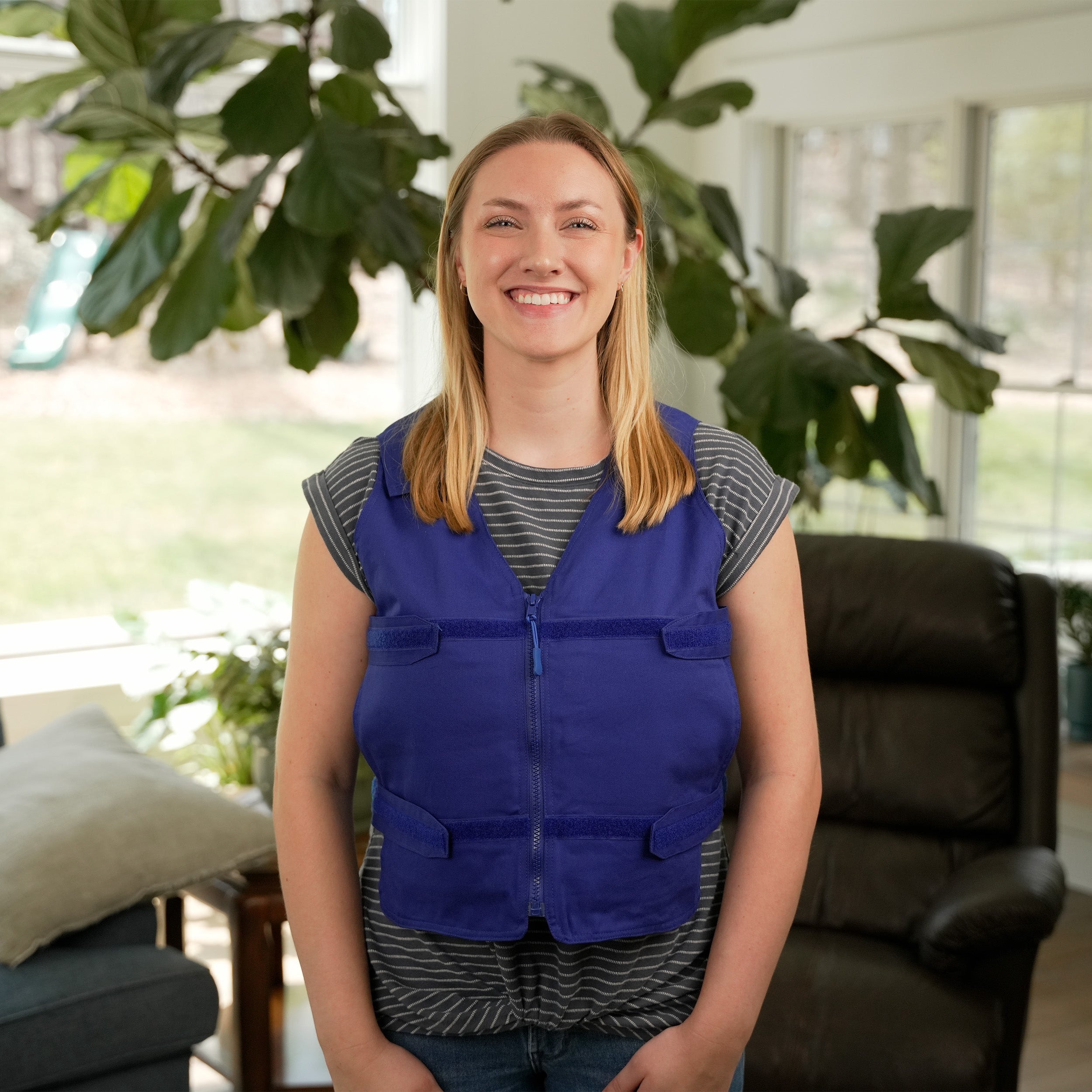 Woman wearing a blue Adjustable Zipper Cooling Vest with Kool Max® packs in a bright living room with plants.