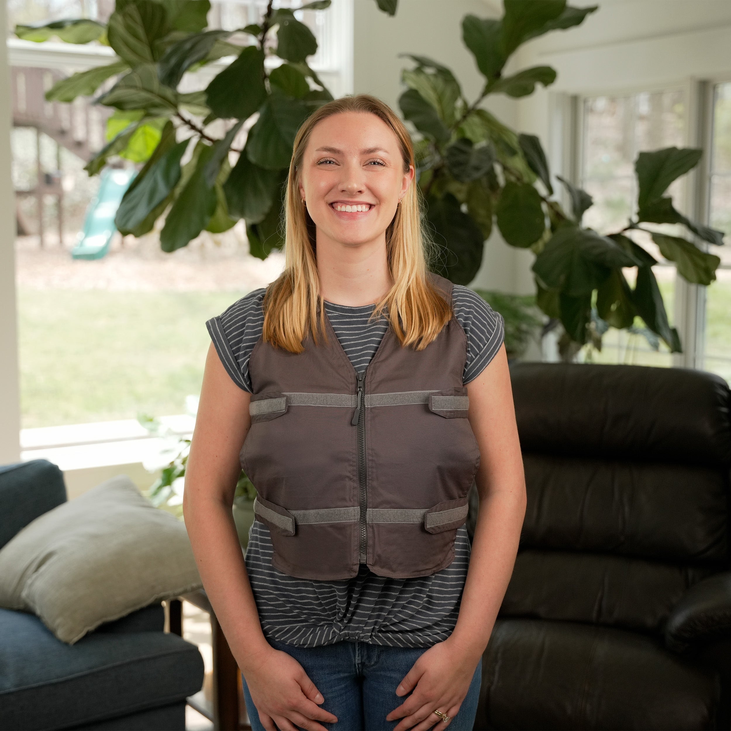 Woman wearing a gray Adjustable Zipper Cooling Vest with Kool Max® Packs in a bright living room with plants in the background.